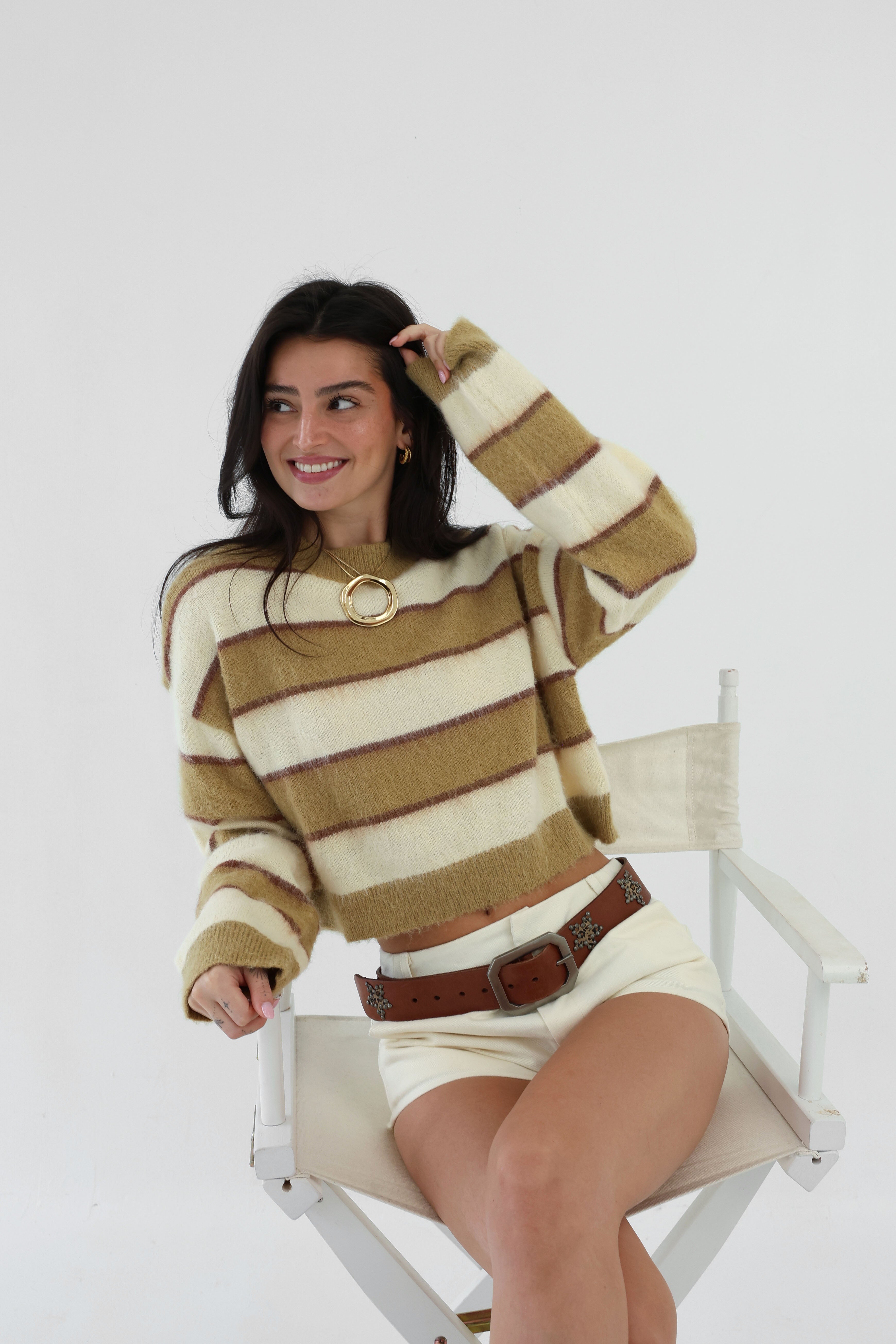 Woman wearing a striped sweater and skirt sitting on a white chair against a white background