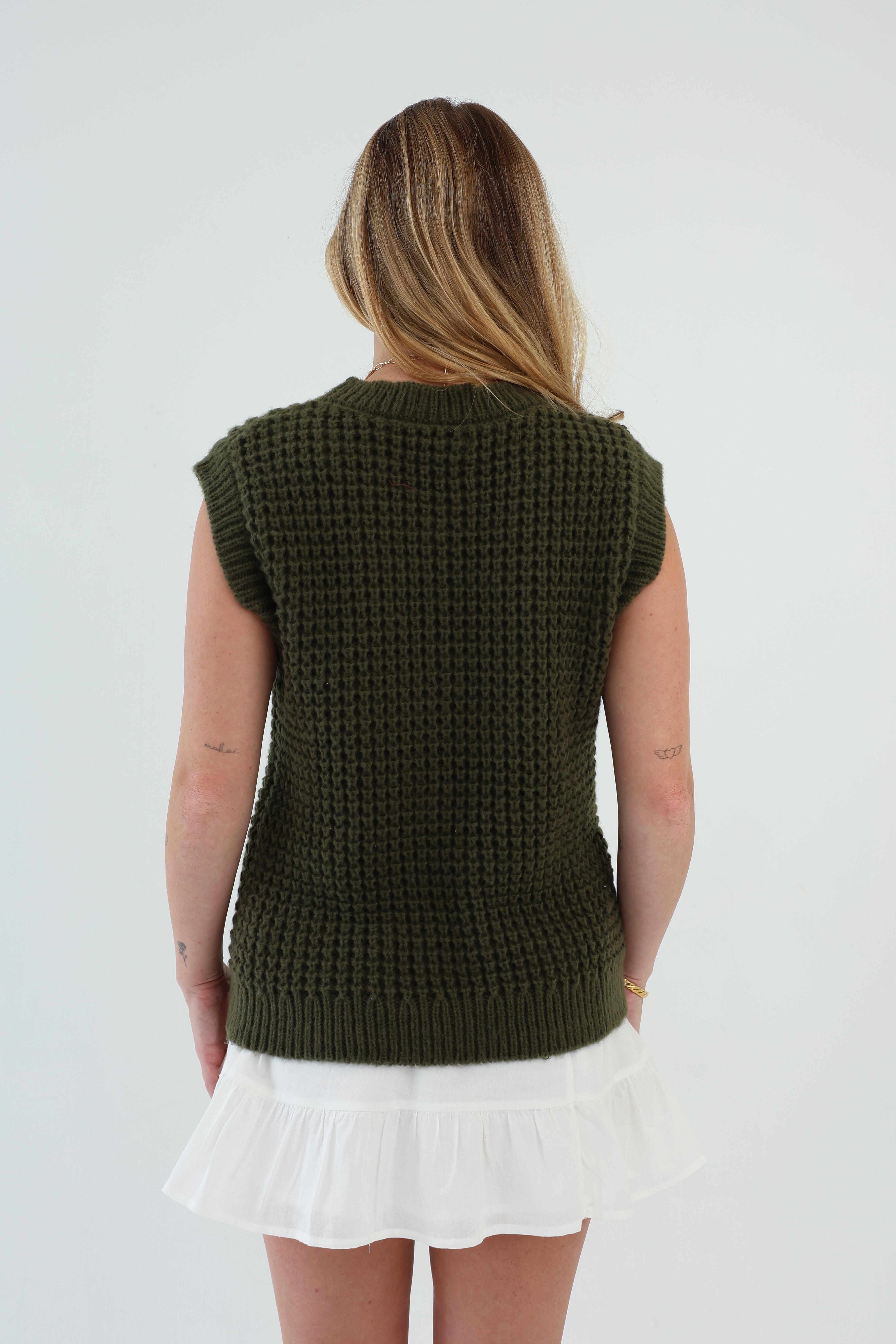 Person wearing a green knitted vest over a white dress on a plain background