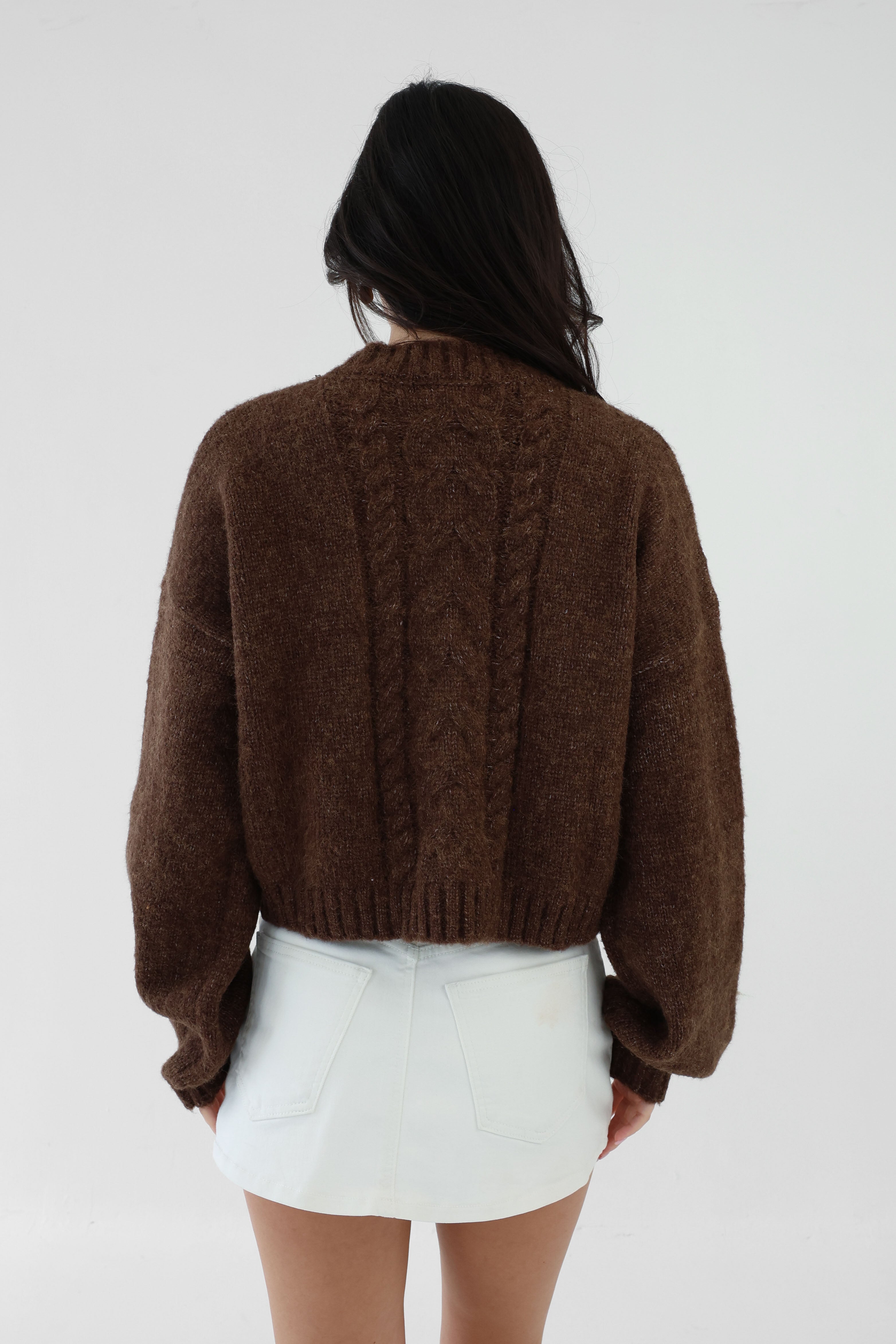 Person wearing a brown cable knit sweater and white shorts on a plain background