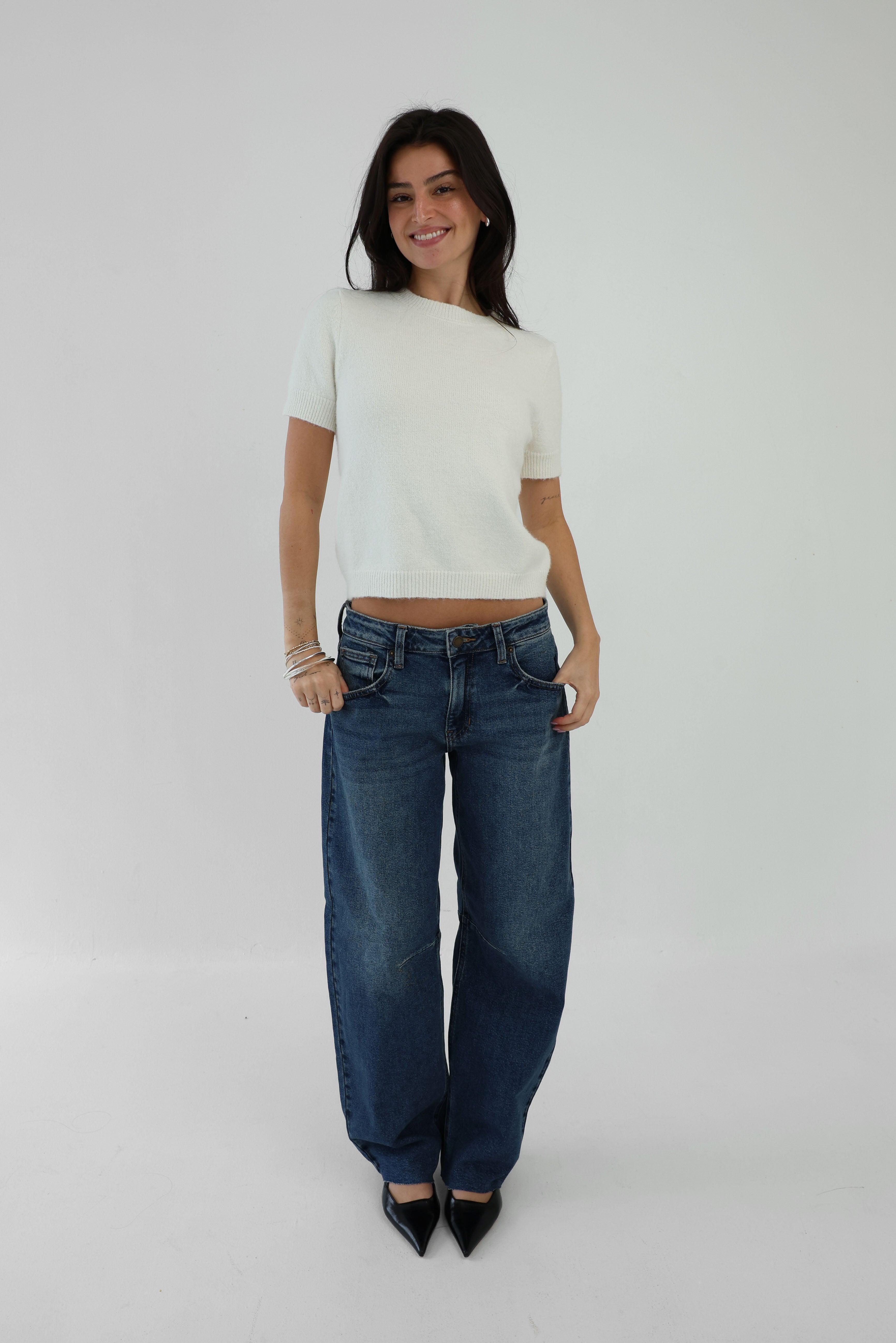 Woman wearing a white top and blue jeans on a plain background