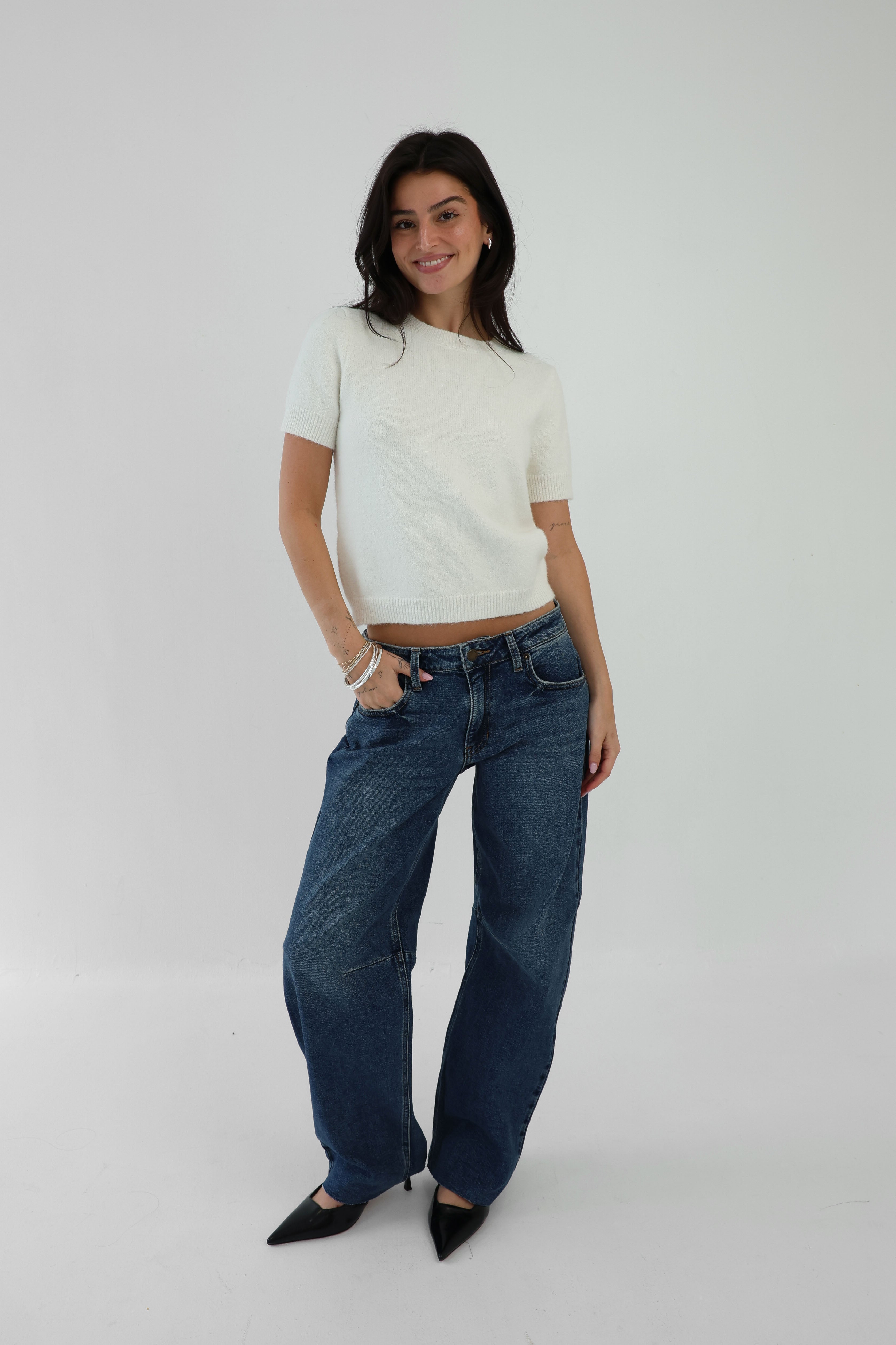 Woman wearing a white top and blue jeans on a plain background