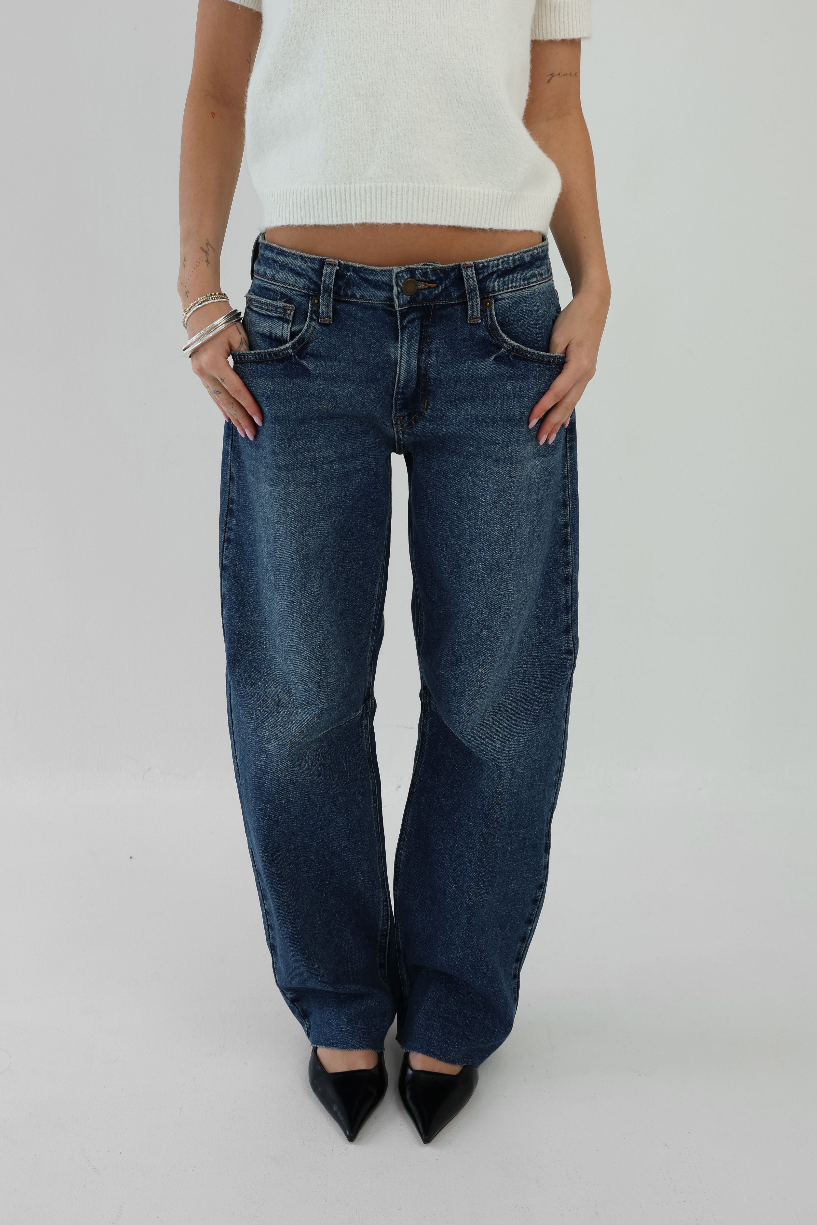 Person wearing blue jeans and a white top on a plain background
