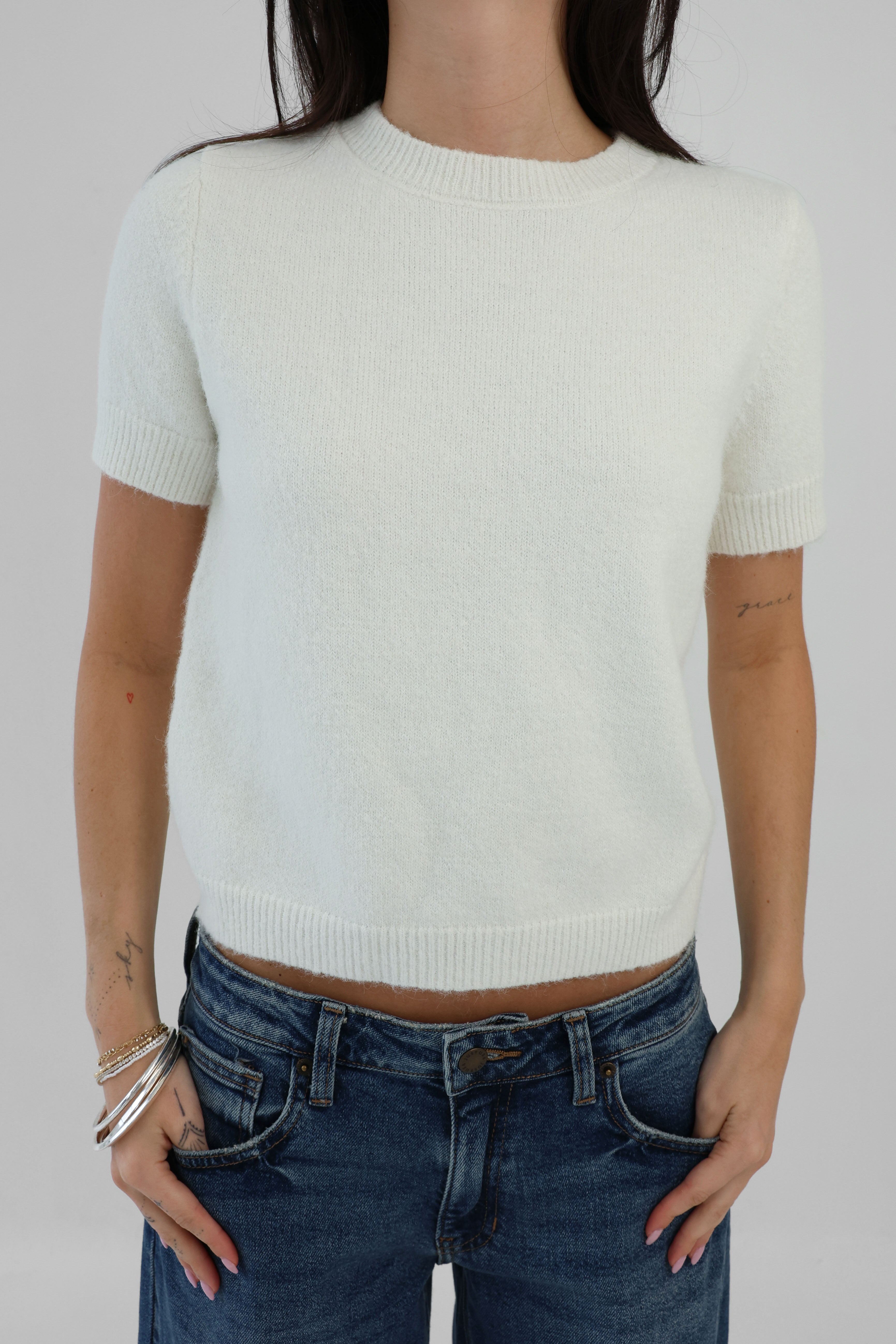 Person wearing a white short-sleeve sweater and blue jeans on a plain background