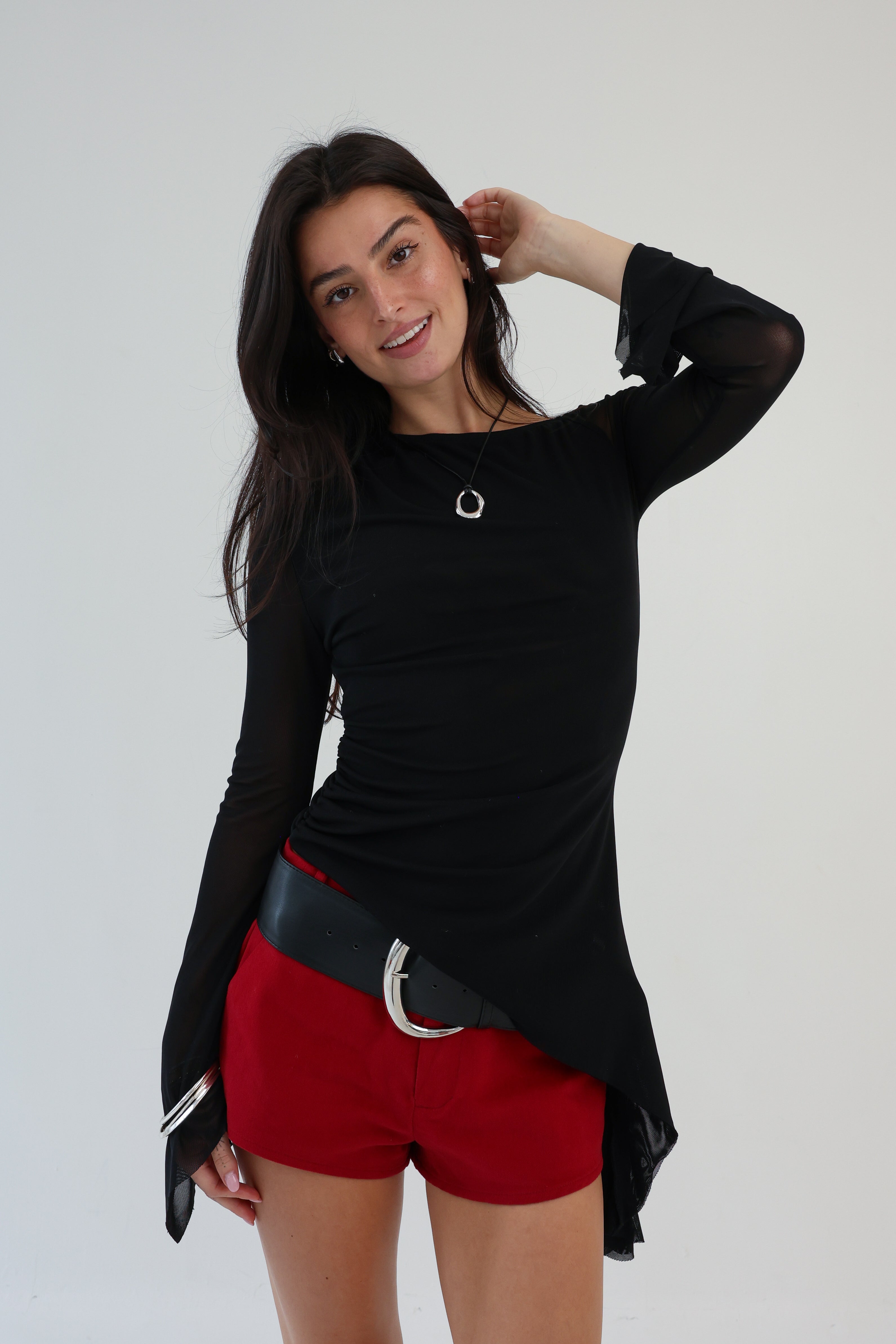 Woman wearing a black long-sleeve top and red shorts against a white background