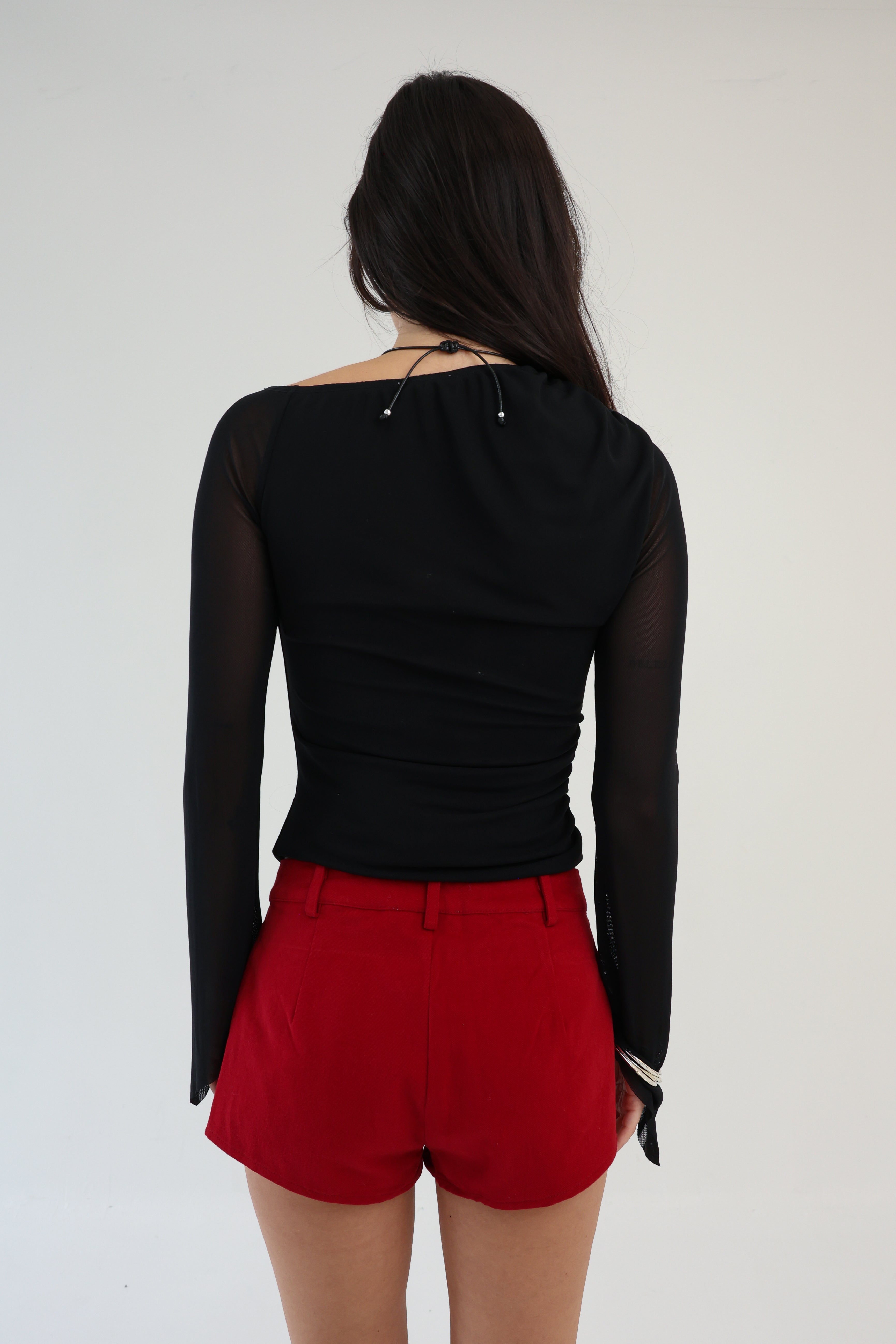 Person wearing a black long-sleeve top and red shorts on a white background