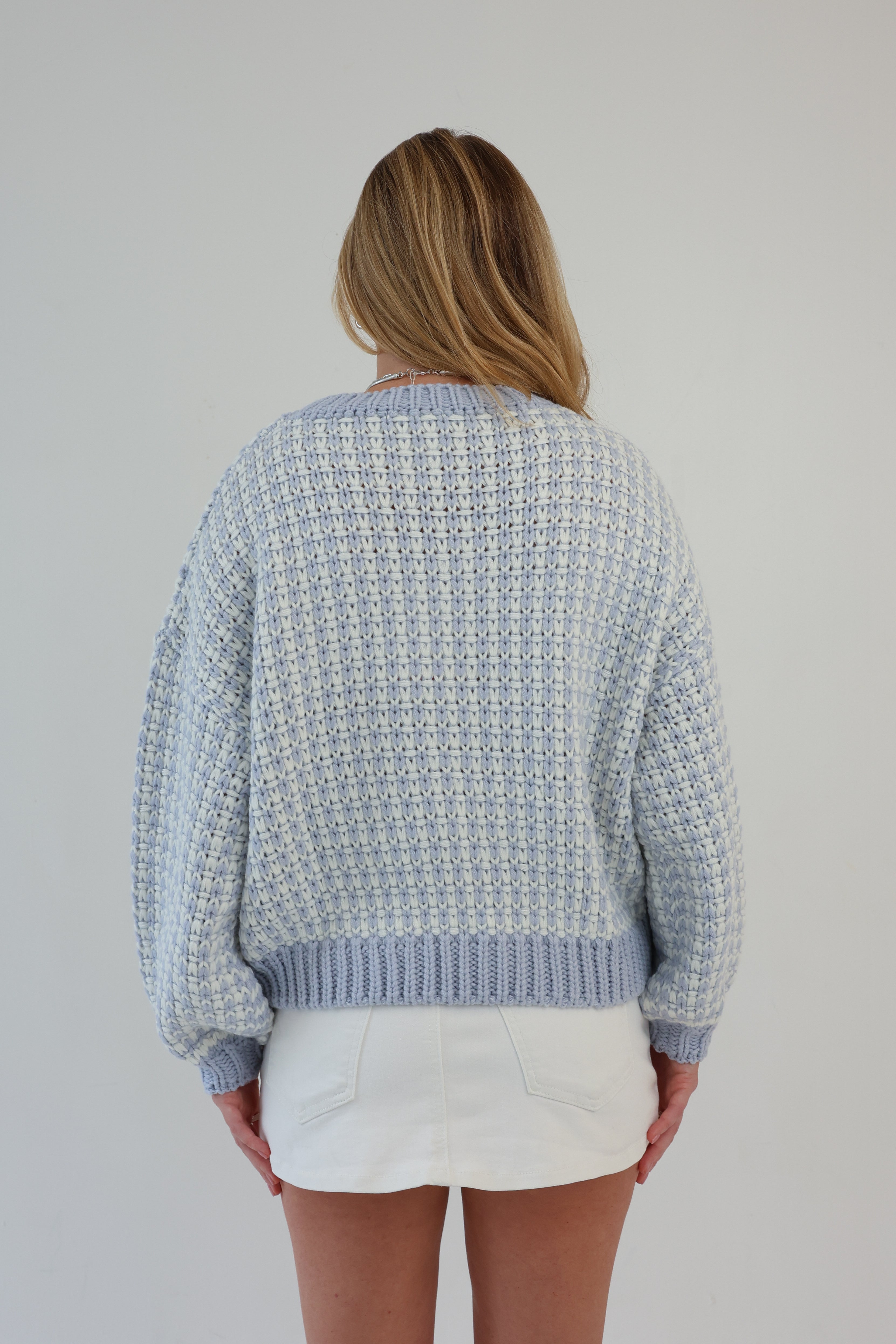 Person wearing a light blue patterned sweater and a white skirt on a plain background
