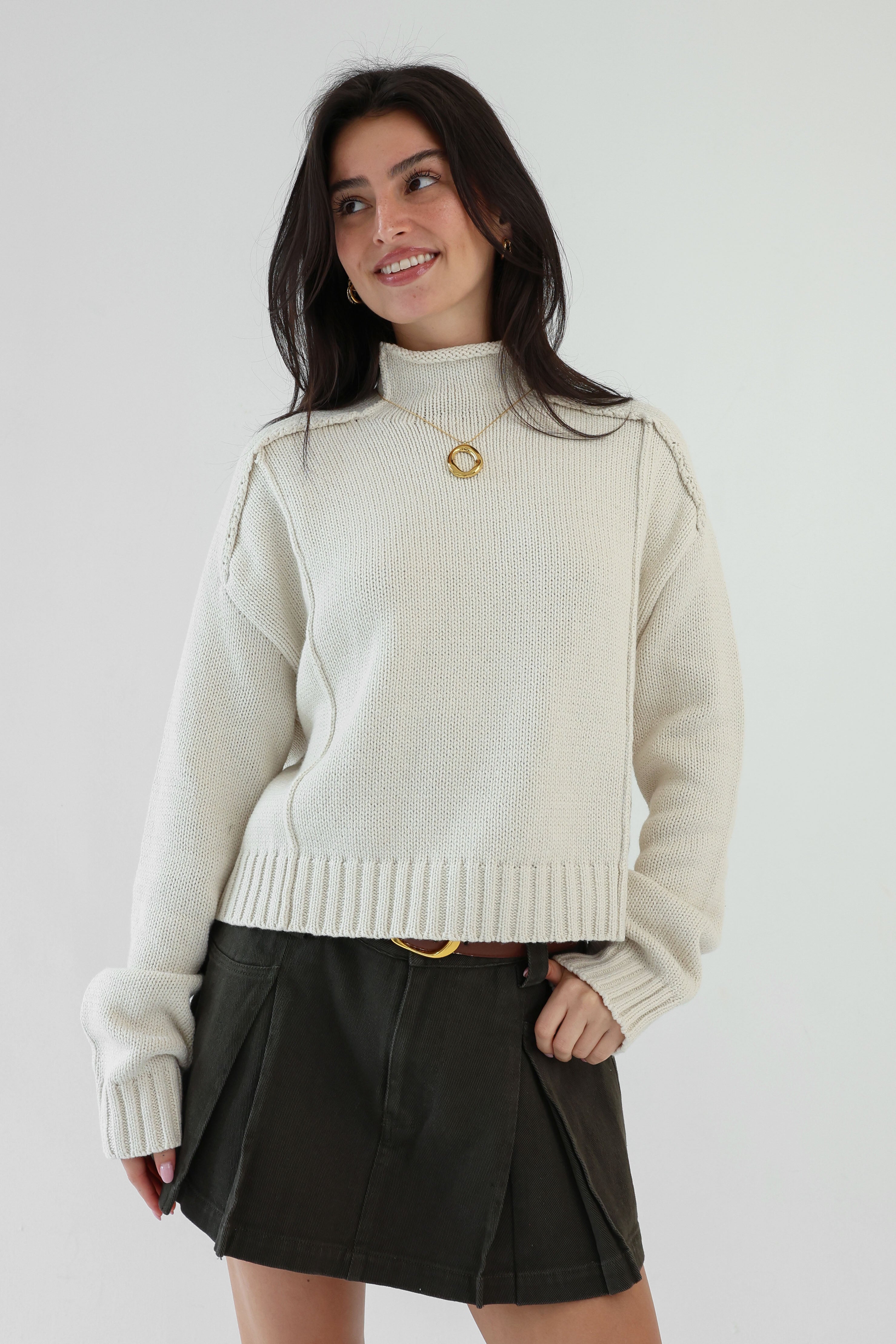 Woman wearing a cream sweater and black skirt against a plain background