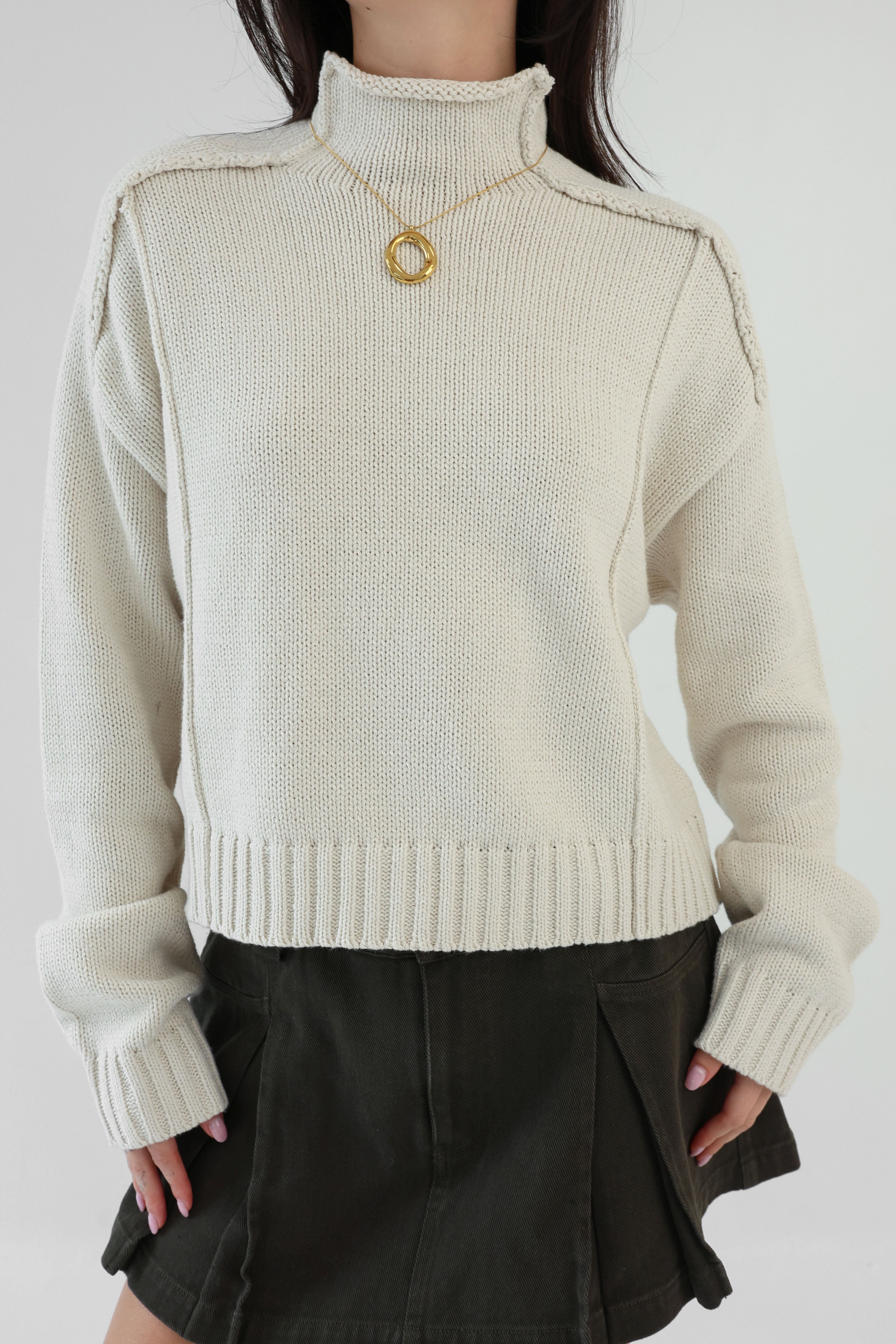 Person wearing a beige knit sweater and black skirt on a white background
