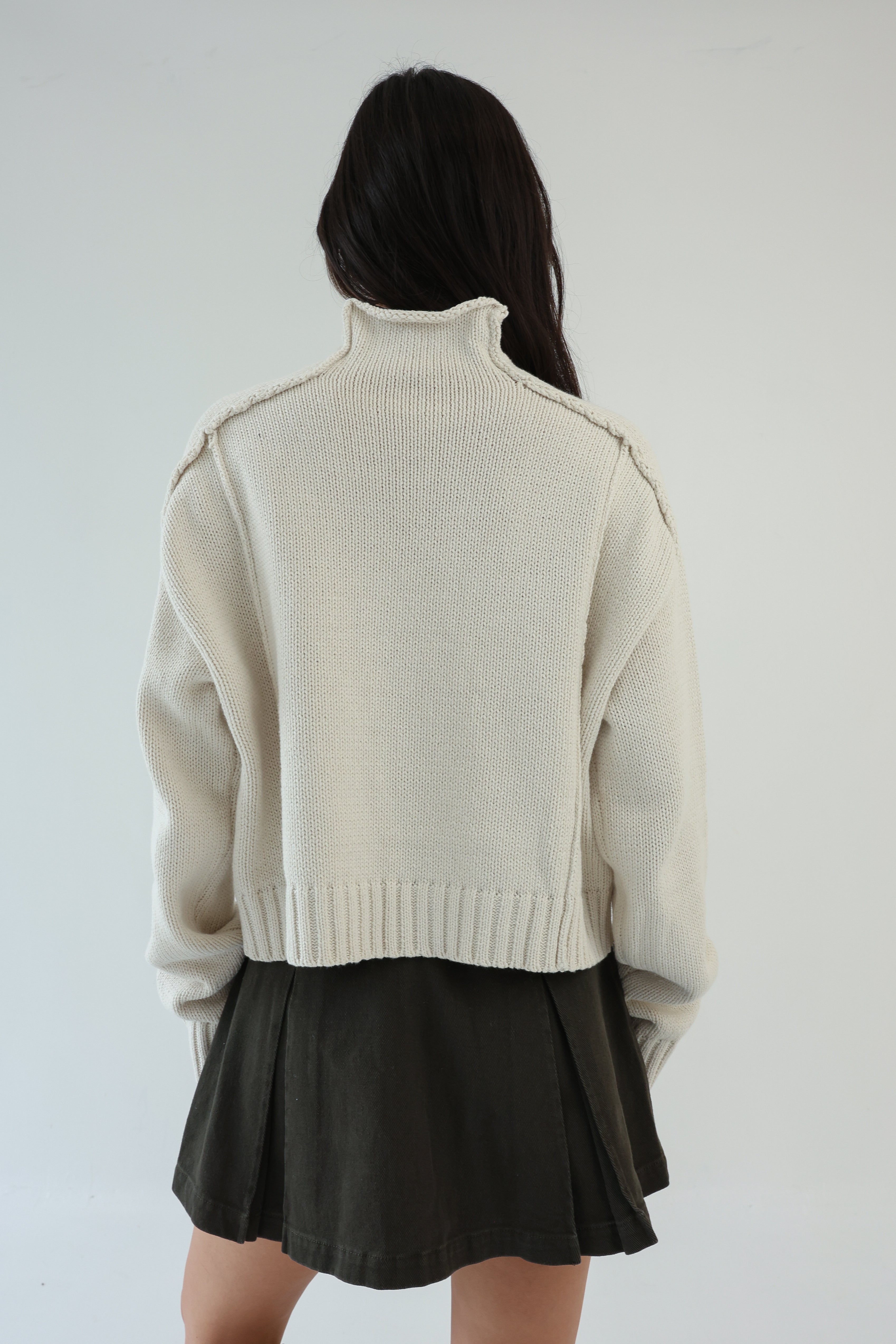 Person wearing a beige sweater and black skirt against a white background