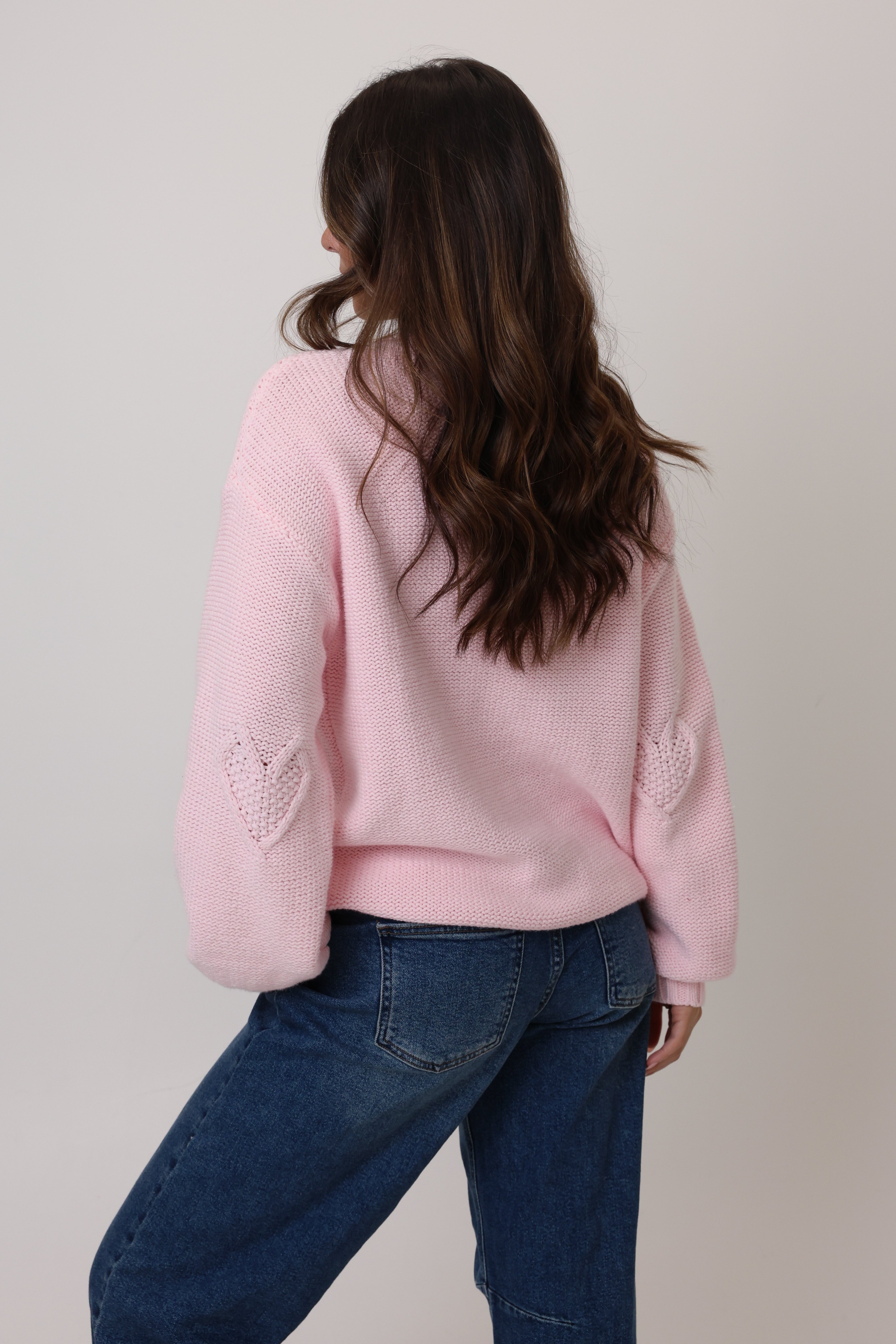 Person wearing a pink sweater with heart designs on a plain background