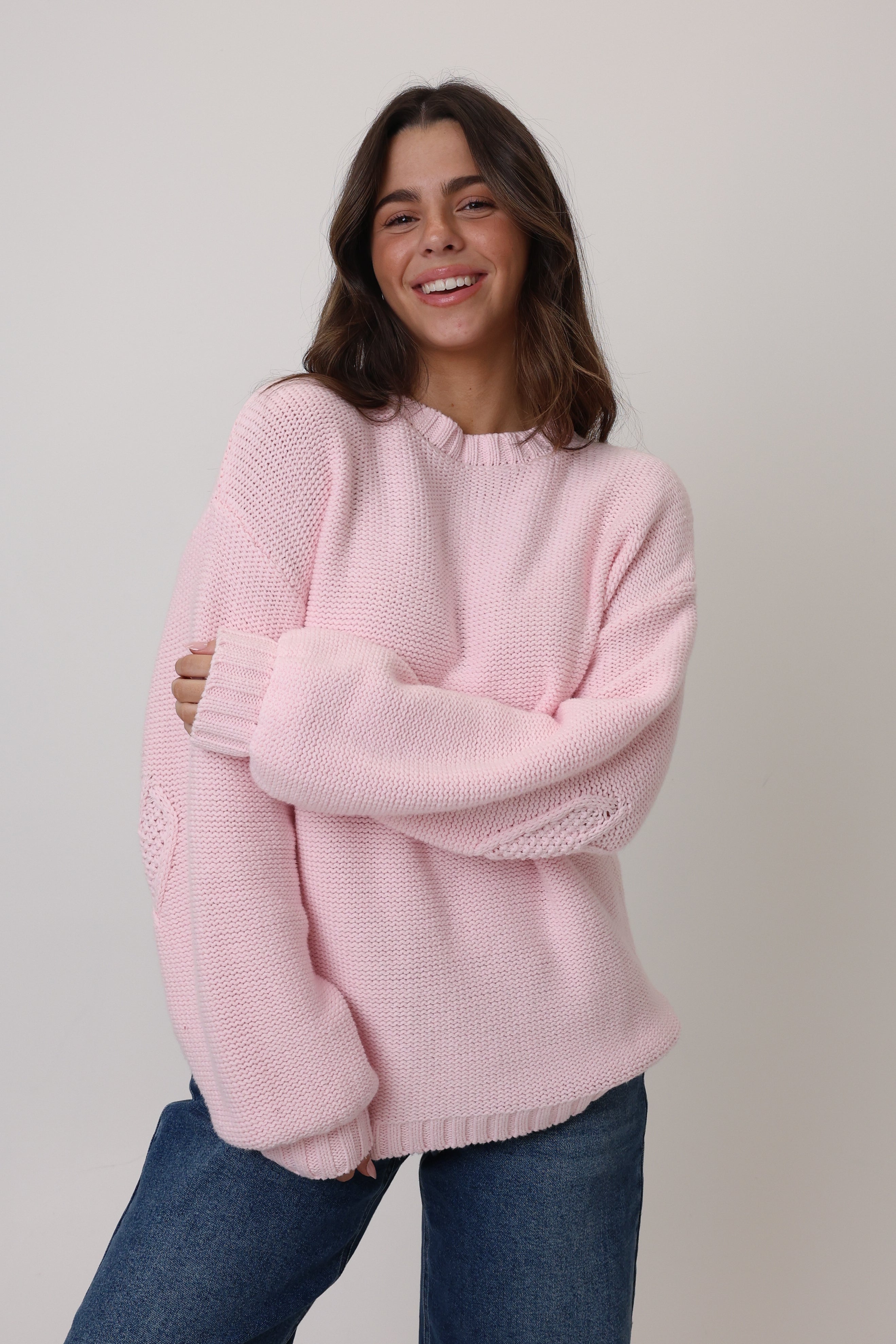 Woman wearing a pink sweater and blue jeans against a plain background