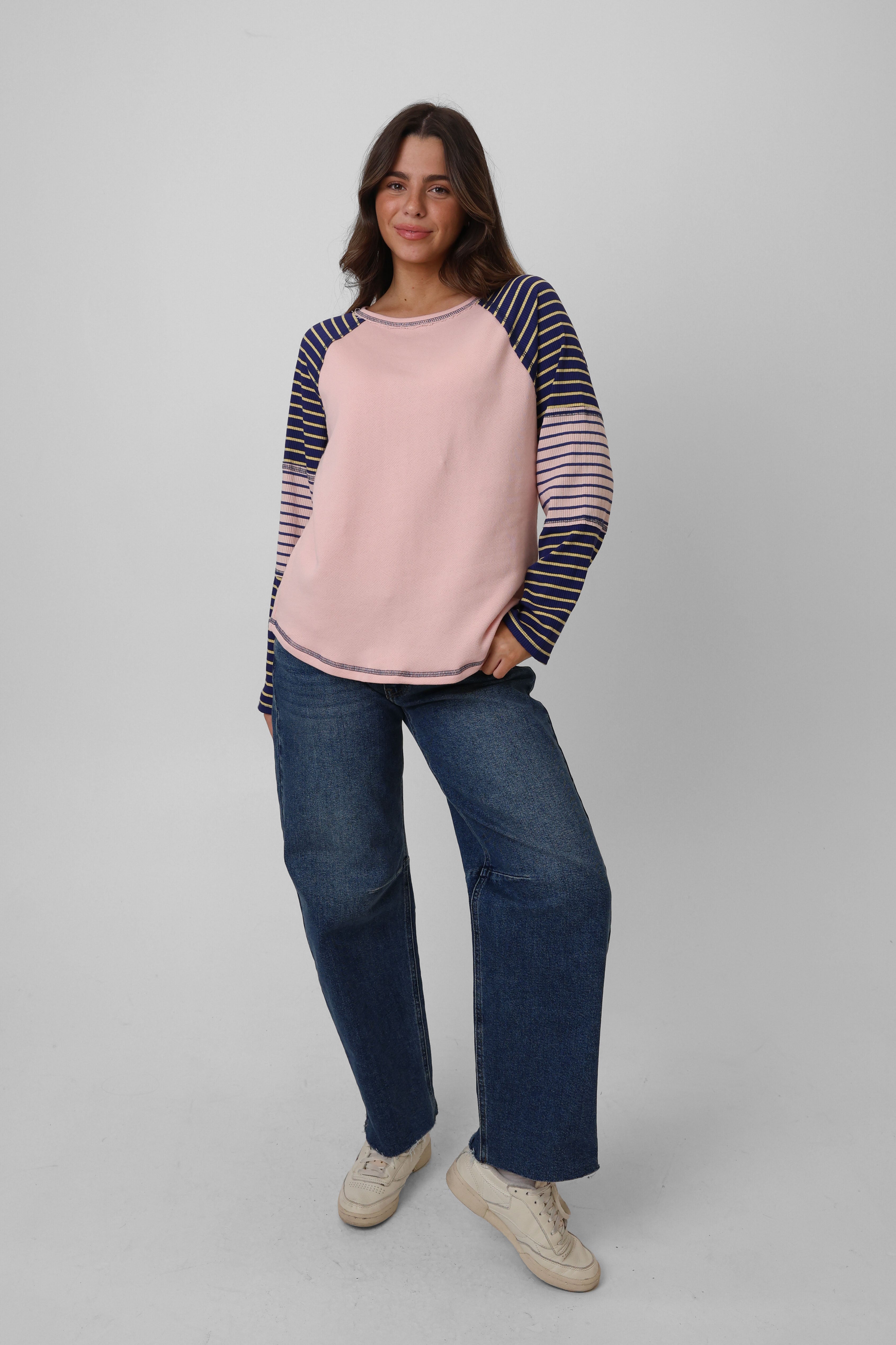 Woman wearing a pink and navy striped sweater with blue jeans on a gray background