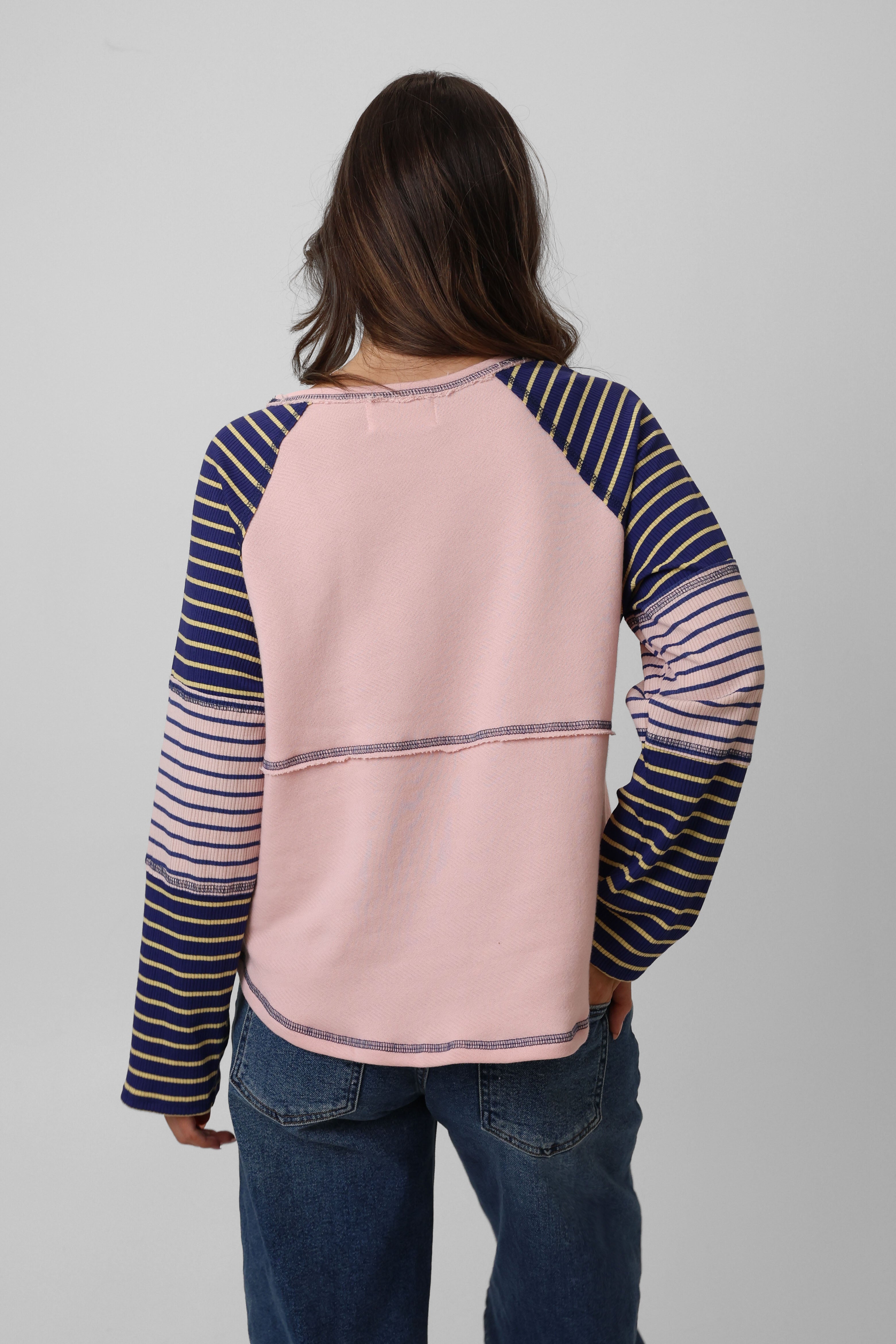 Person wearing a pink and navy striped long-sleeve shirt with sheer sleeves on a gray background