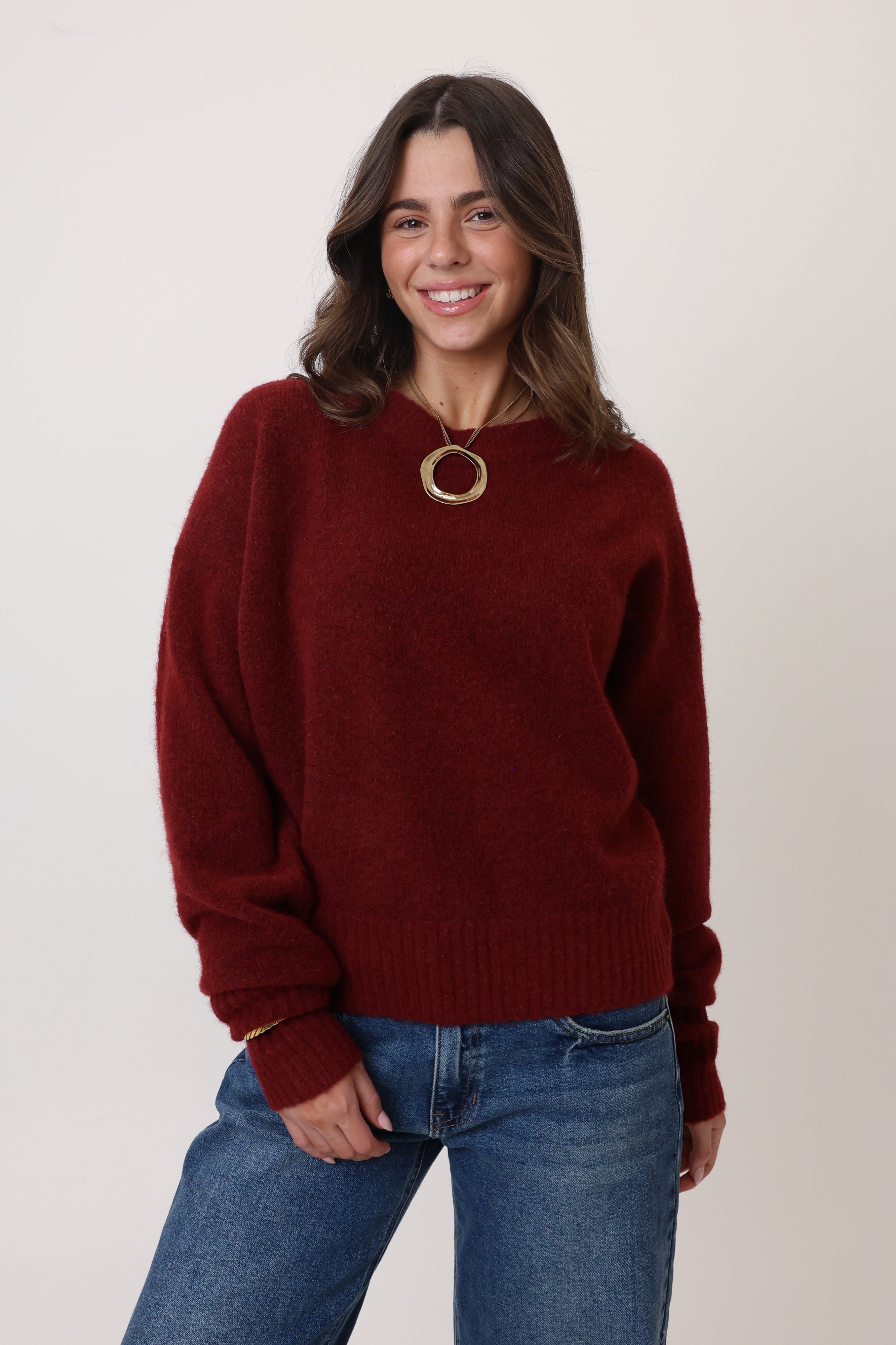 Woman wearing a burgundy sweater and blue jeans against a white background