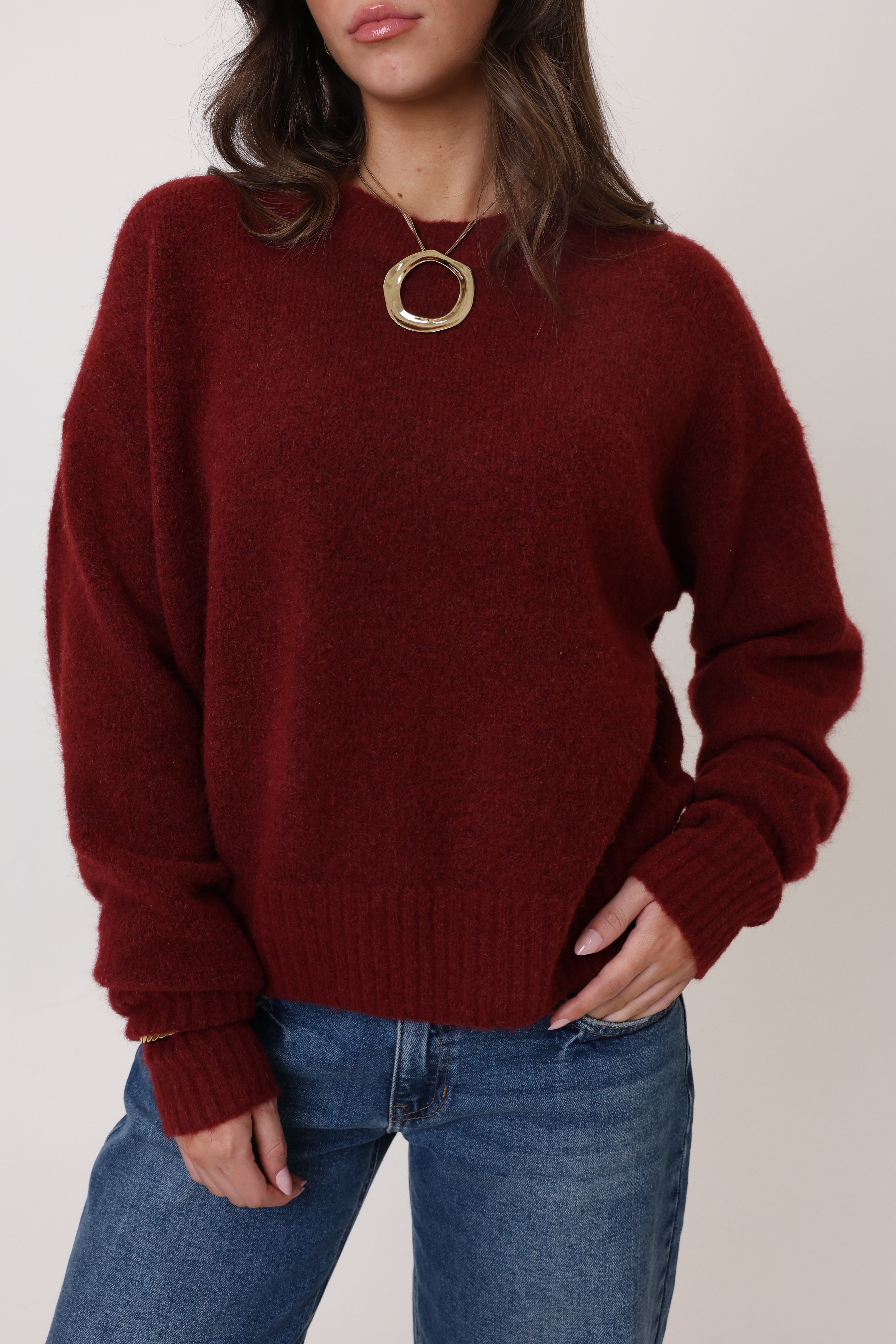 Person wearing a burgundy sweater and blue jeans against a plain background