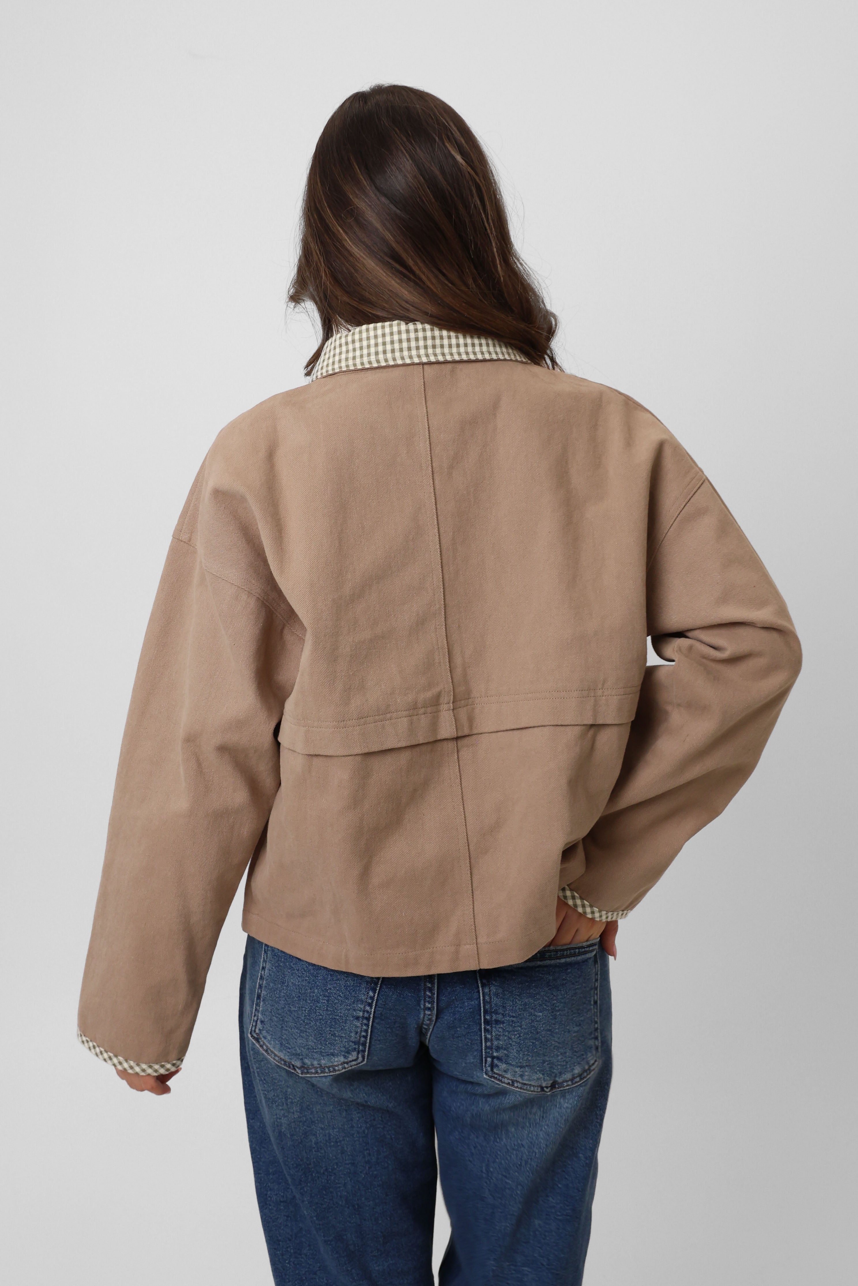 Person wearing a beige jacket and blue jeans on a white background