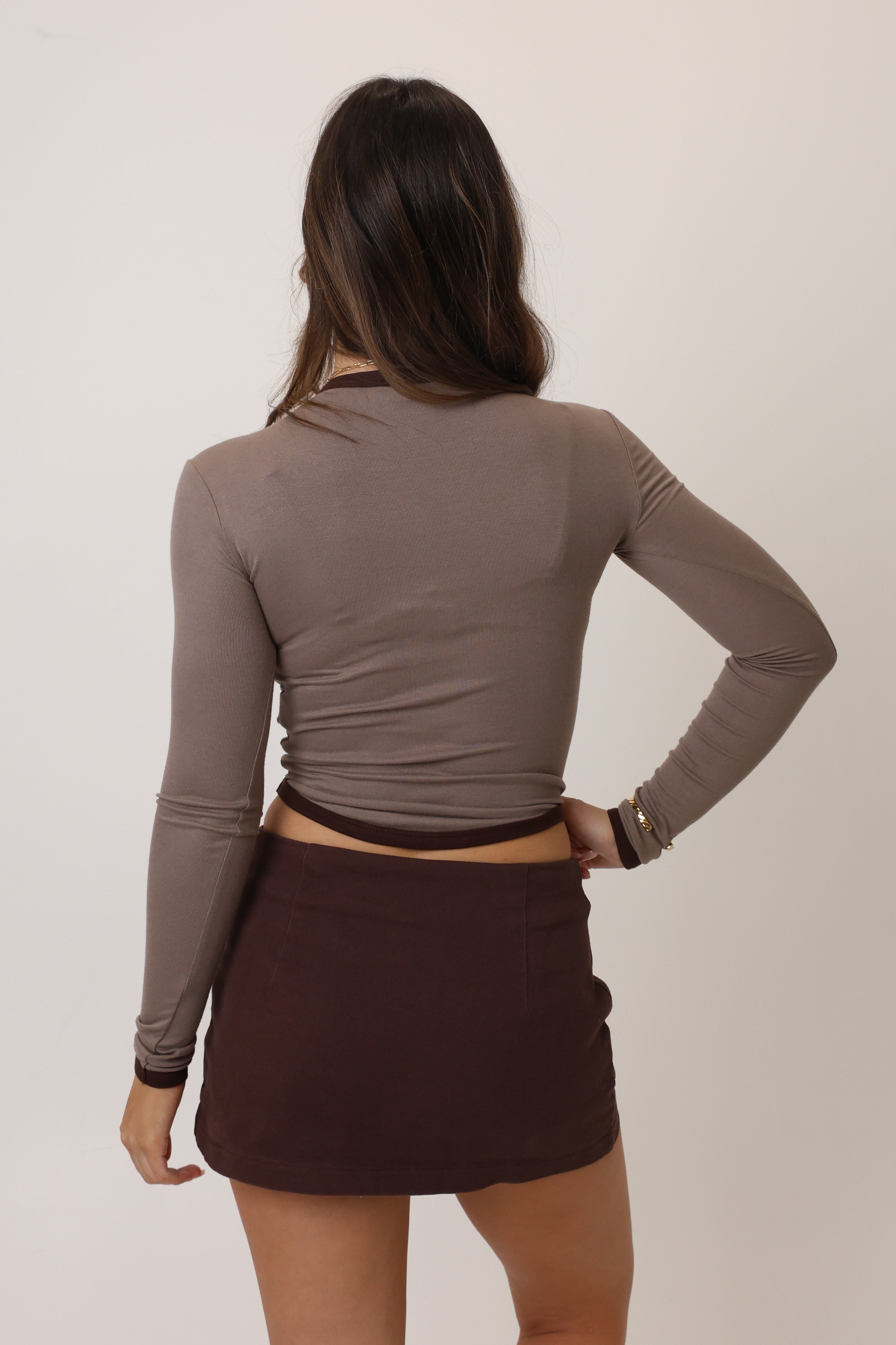 Woman wearing a brown long-sleeve top and skirt against a plain background