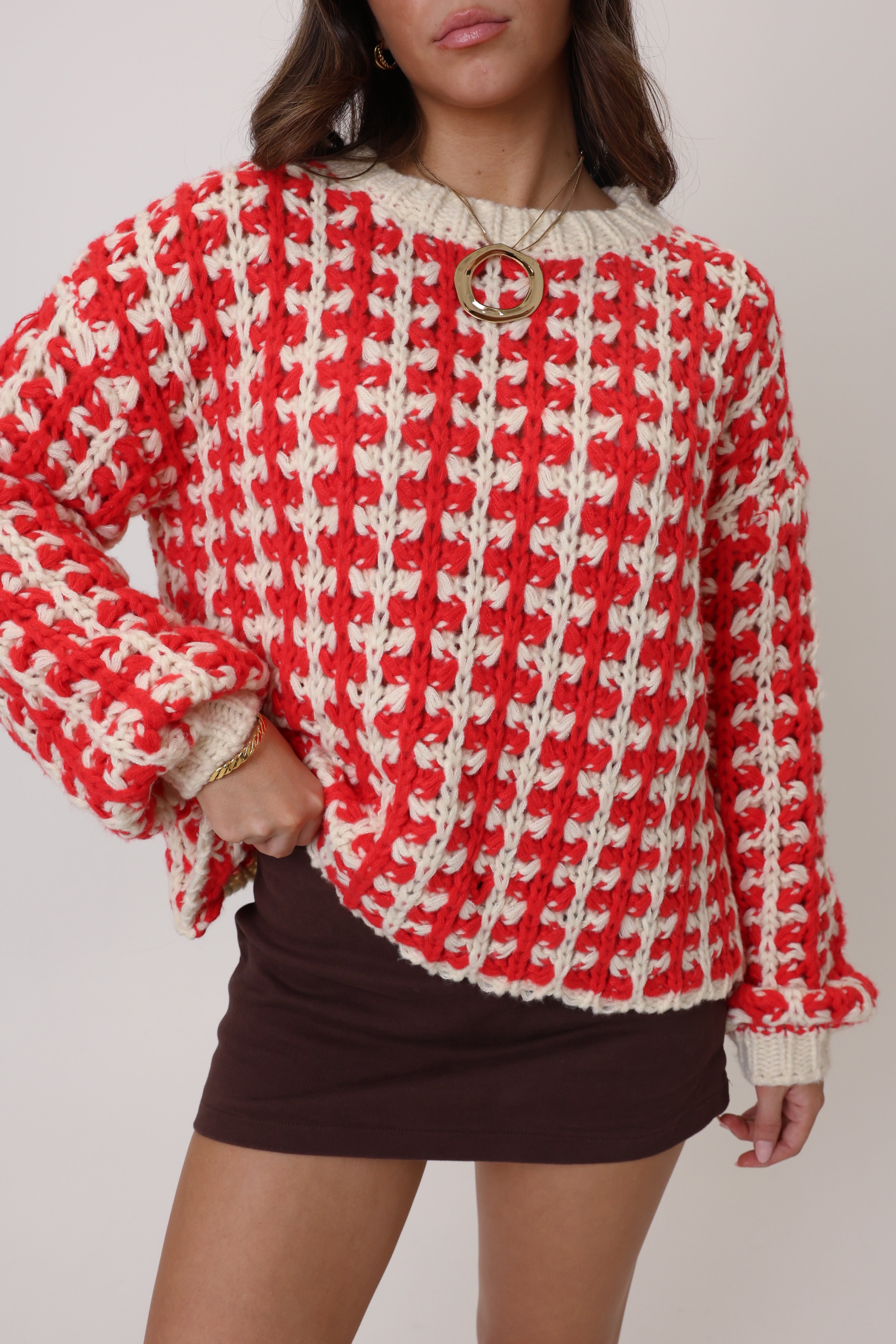 Person wearing a red and white houndstooth pattern sweater with a plain background