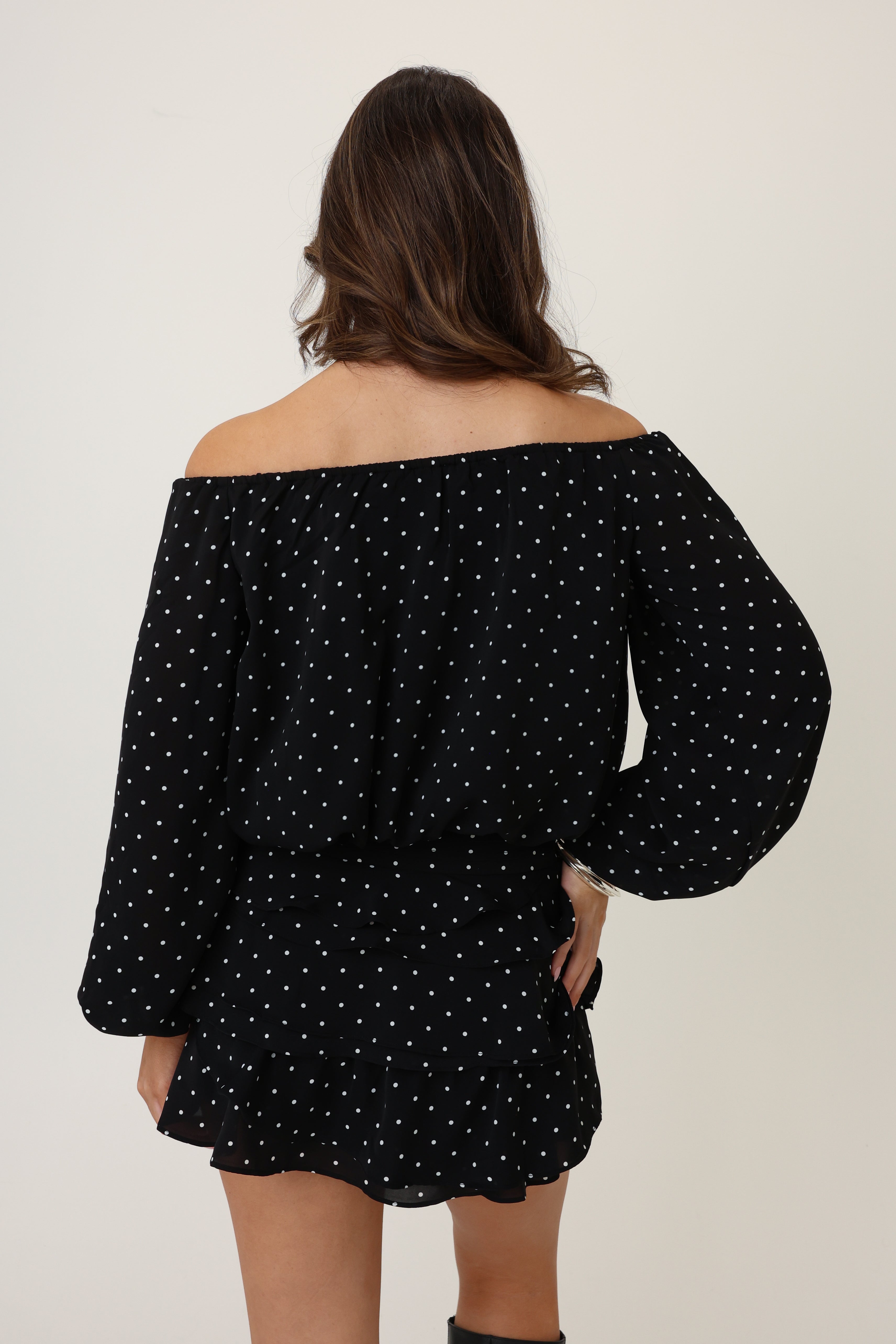 Person wearing a black off-shoulder top with white polka dots on a plain background