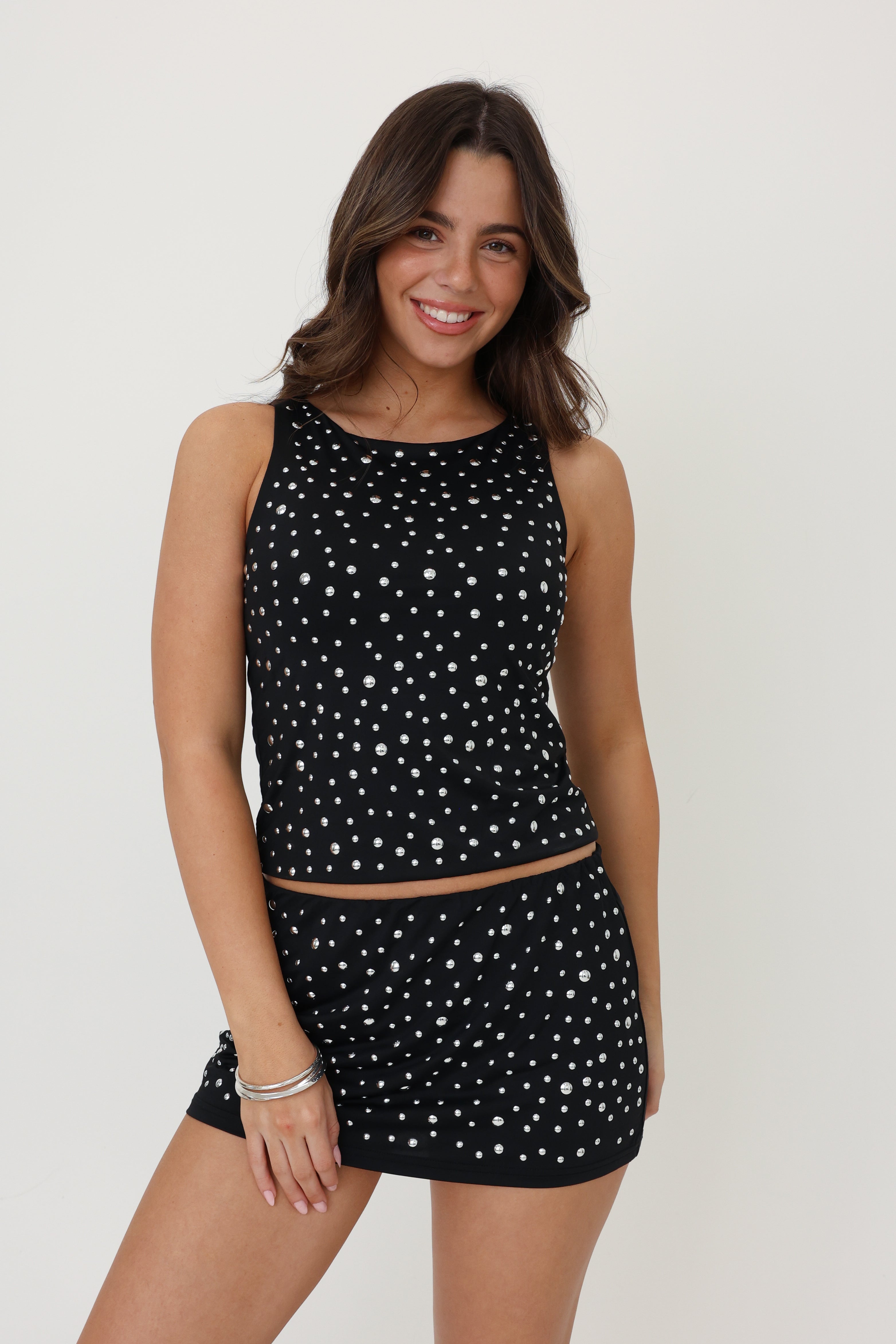 Woman wearing a black sleeveless top and skirt with white polka dots on a plain background