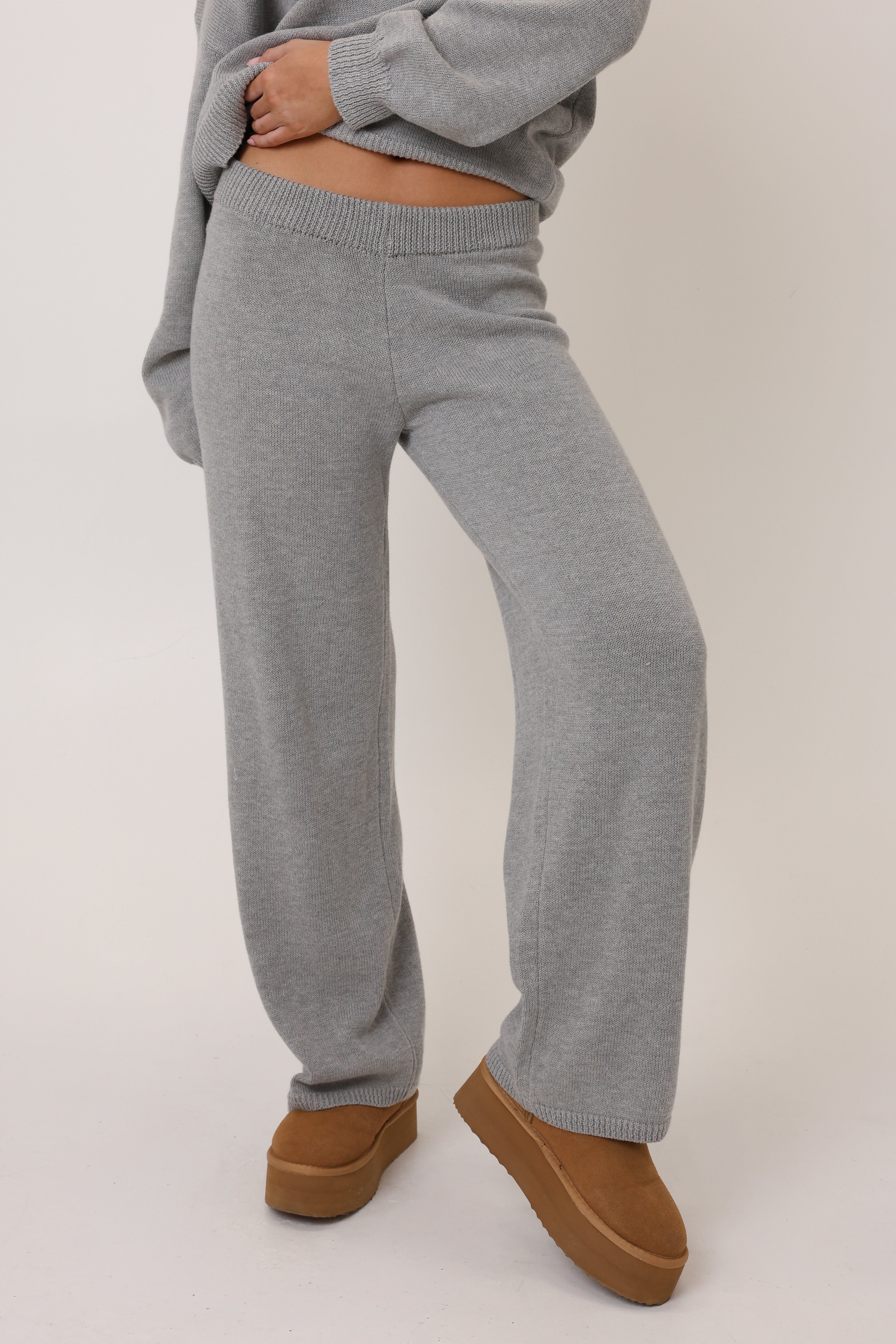 Person wearing gray ribbed knit pants and brown shoes on a white background
