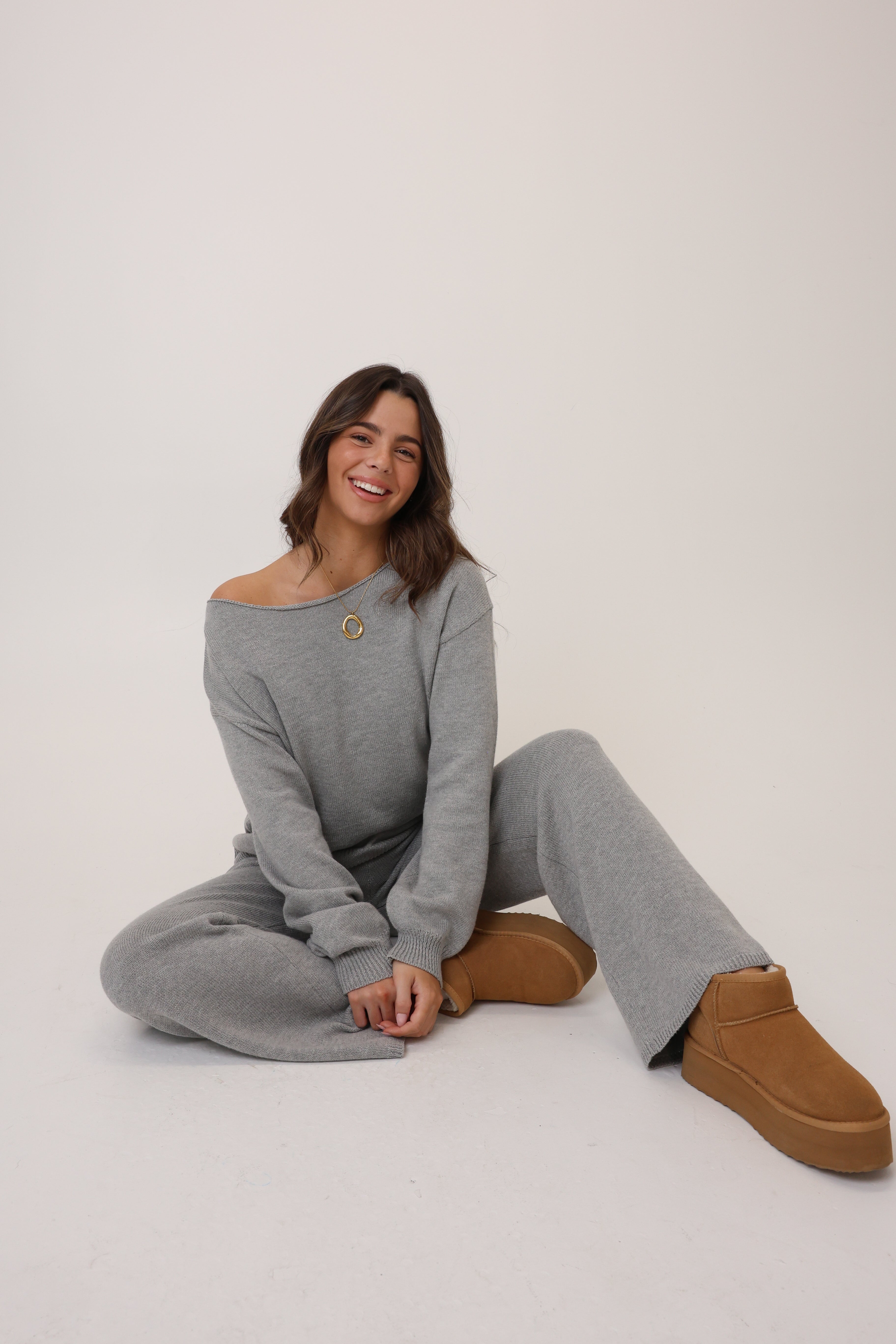 Woman wearing a gray outfit with brown boots sitting on a white background