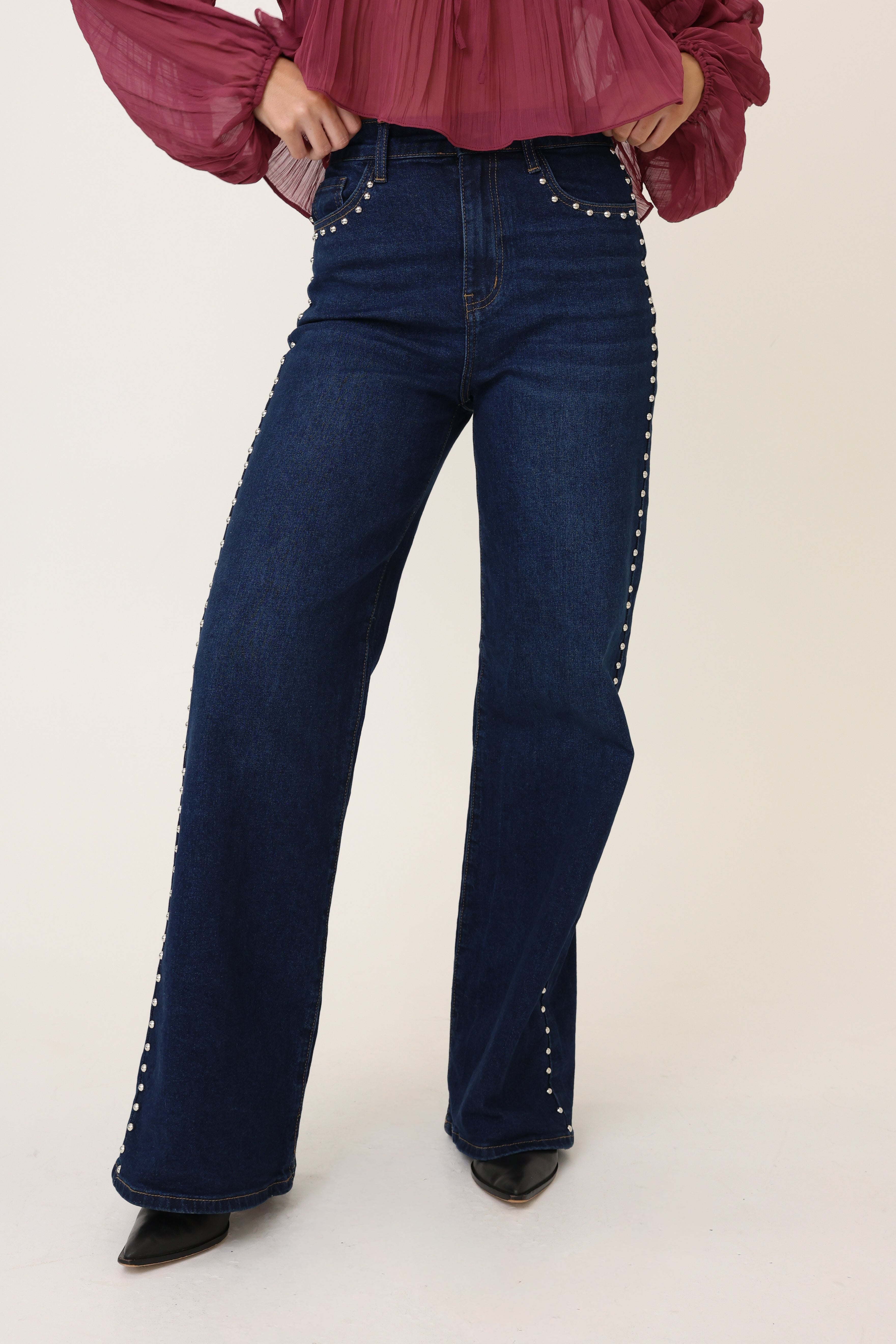 Person wearing blue jeans with decorative studs on a white background