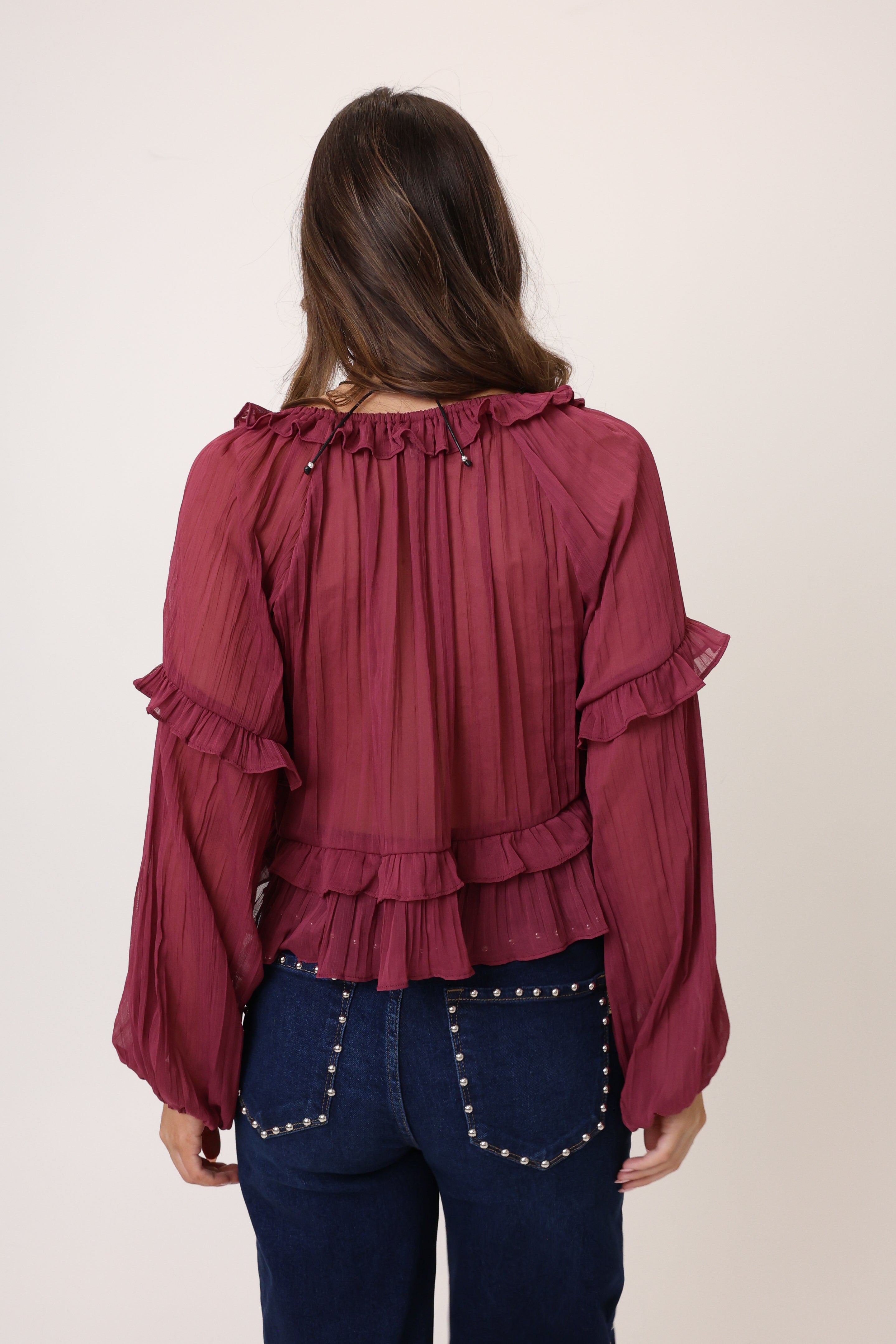 Person wearing a burgundy blouse with ruffled details on a plain background