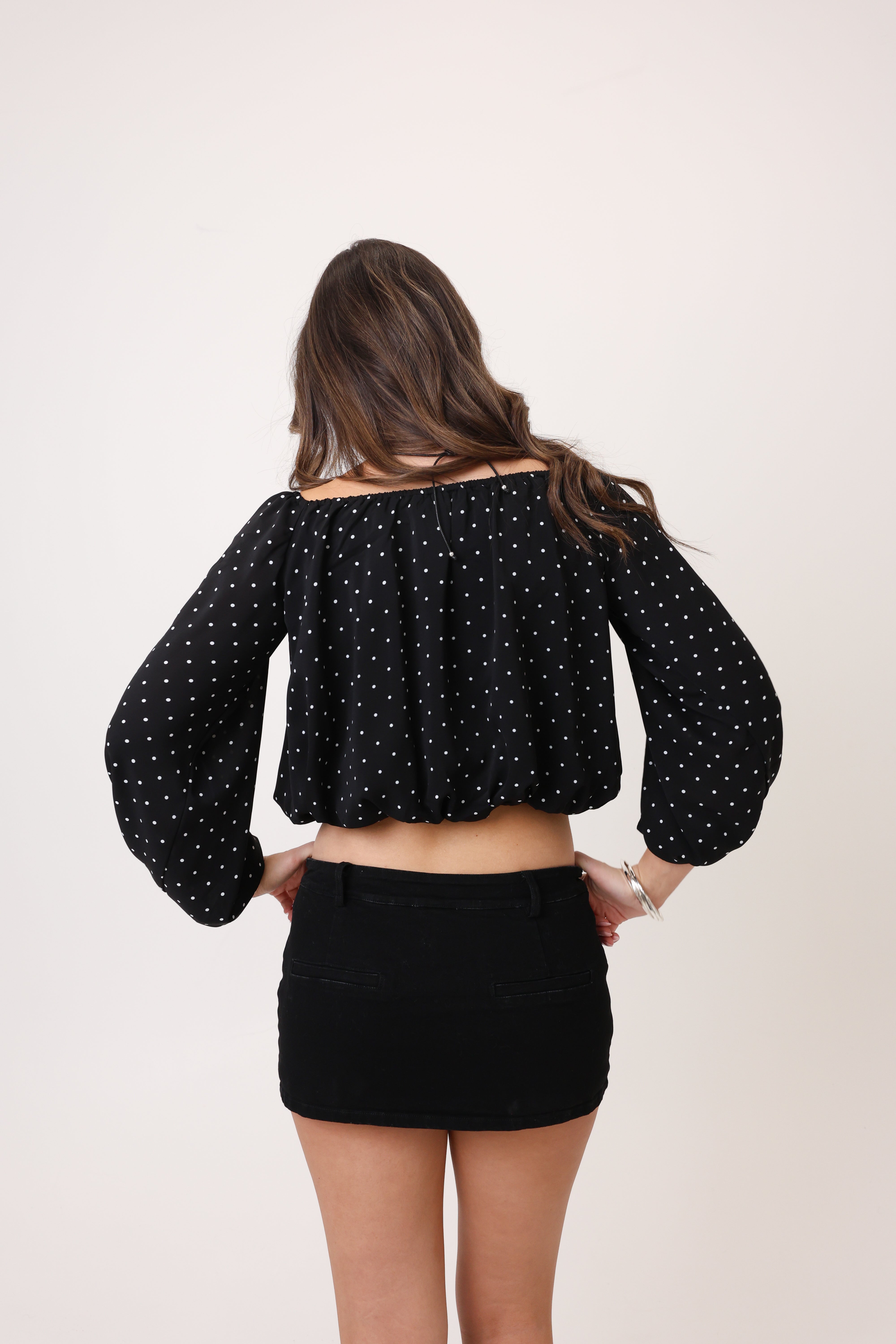 Person wearing a black polka dot blouse and black skirt on a white background