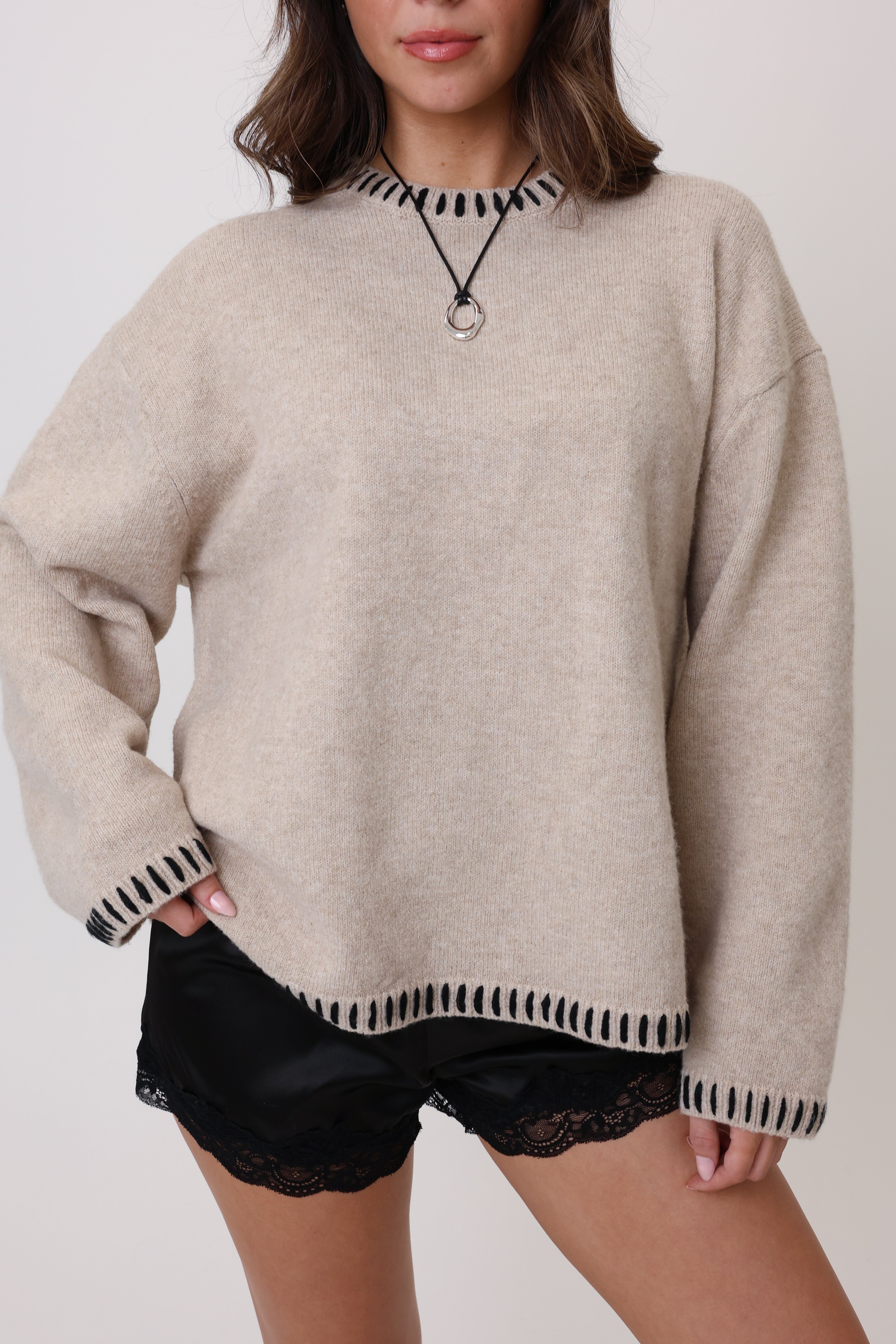 Person wearing a beige sweater with black trim and black shorts on a plain background