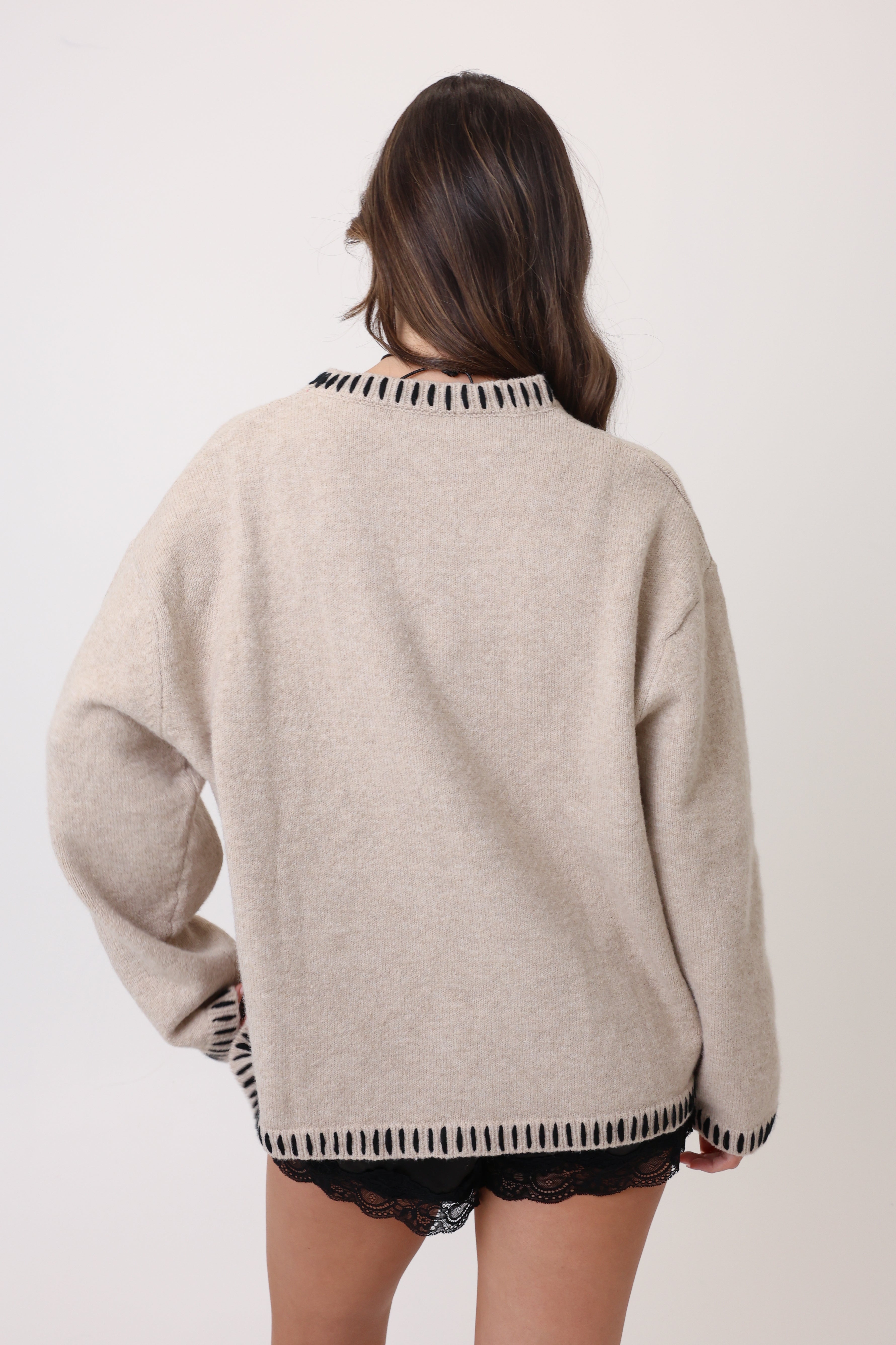 Beige sweater with black and white patterned trim worn by a person on a plain background