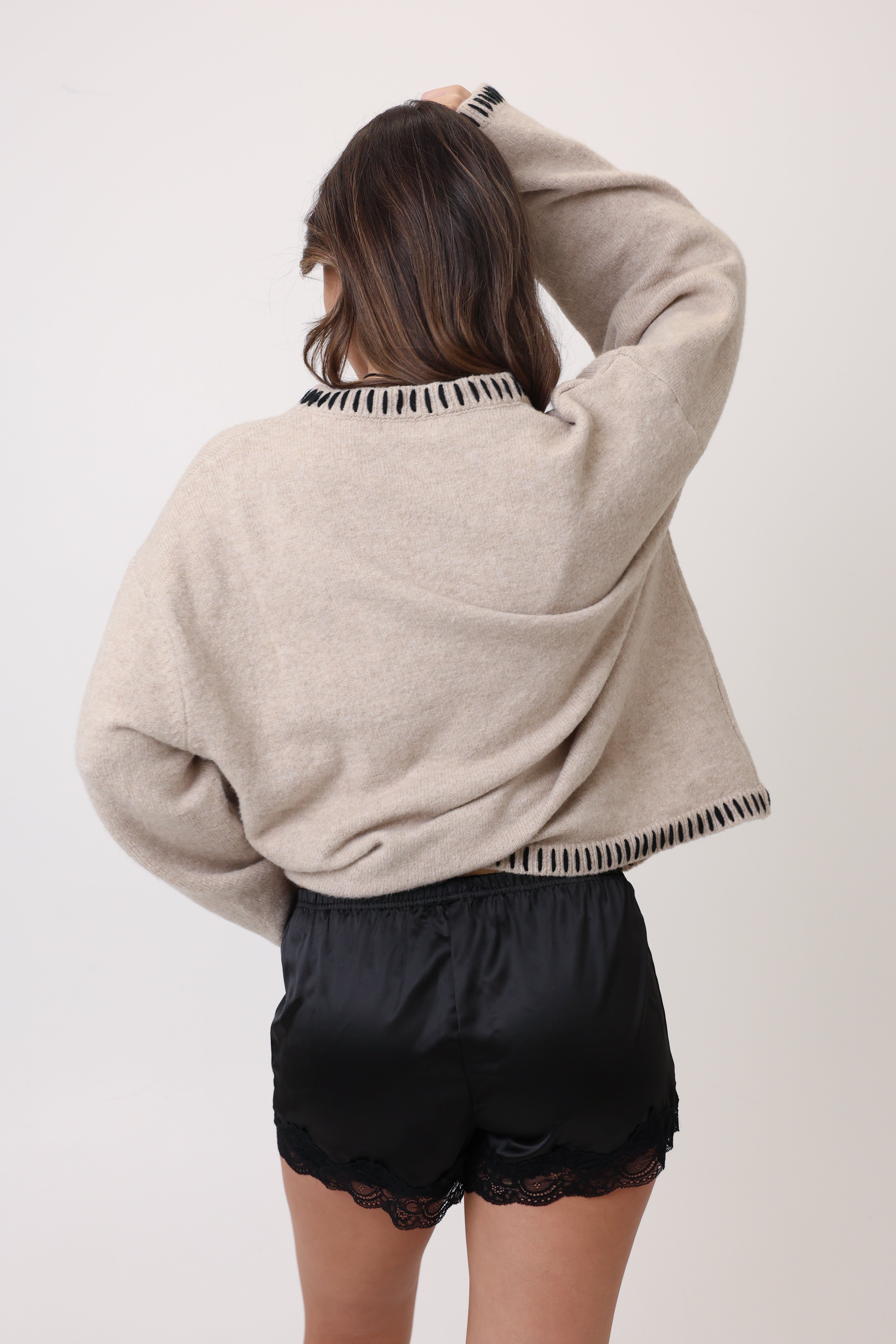 Person wearing a beige sweater and black shorts on a white background