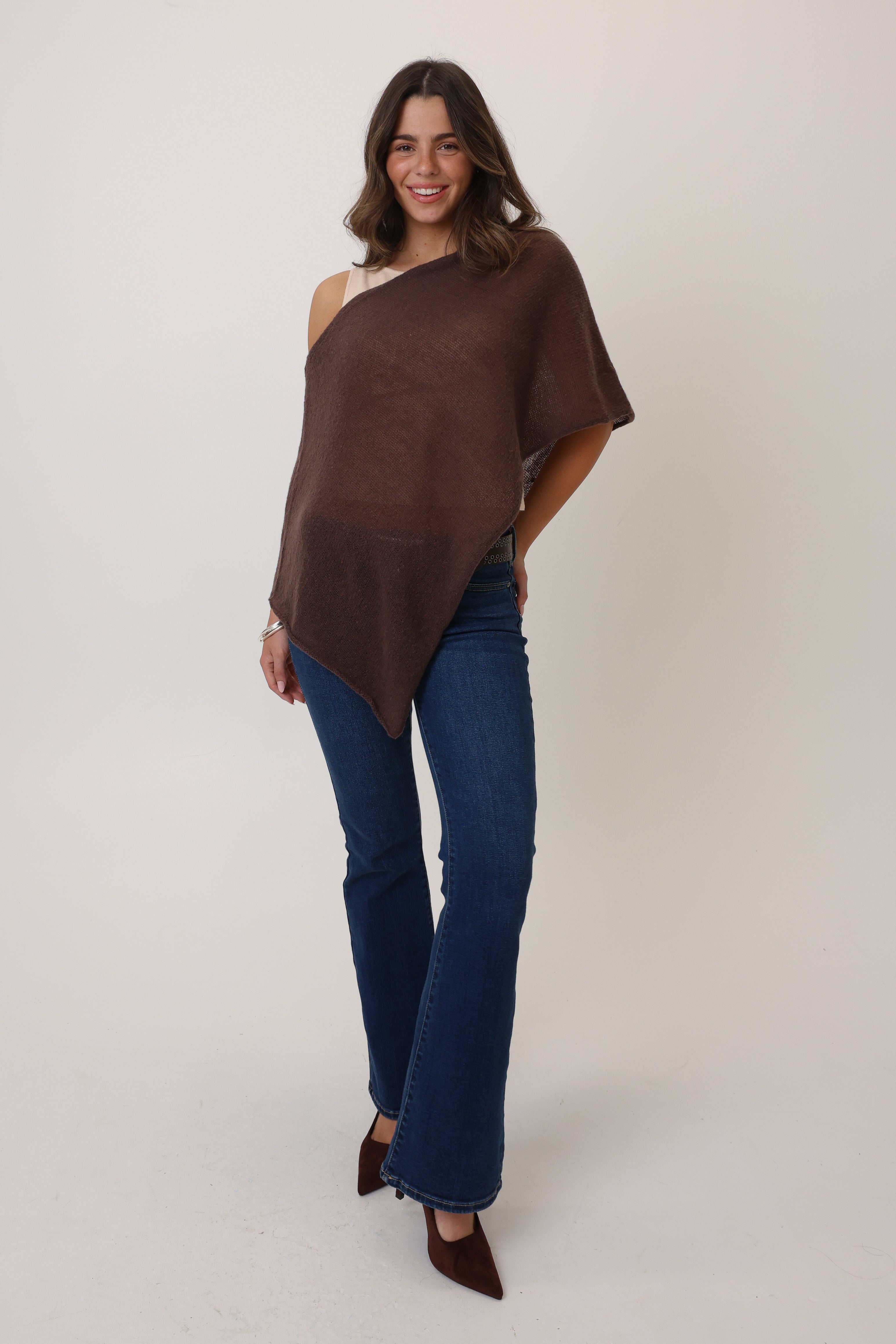 Woman wearing a brown poncho and blue jeans on a white background