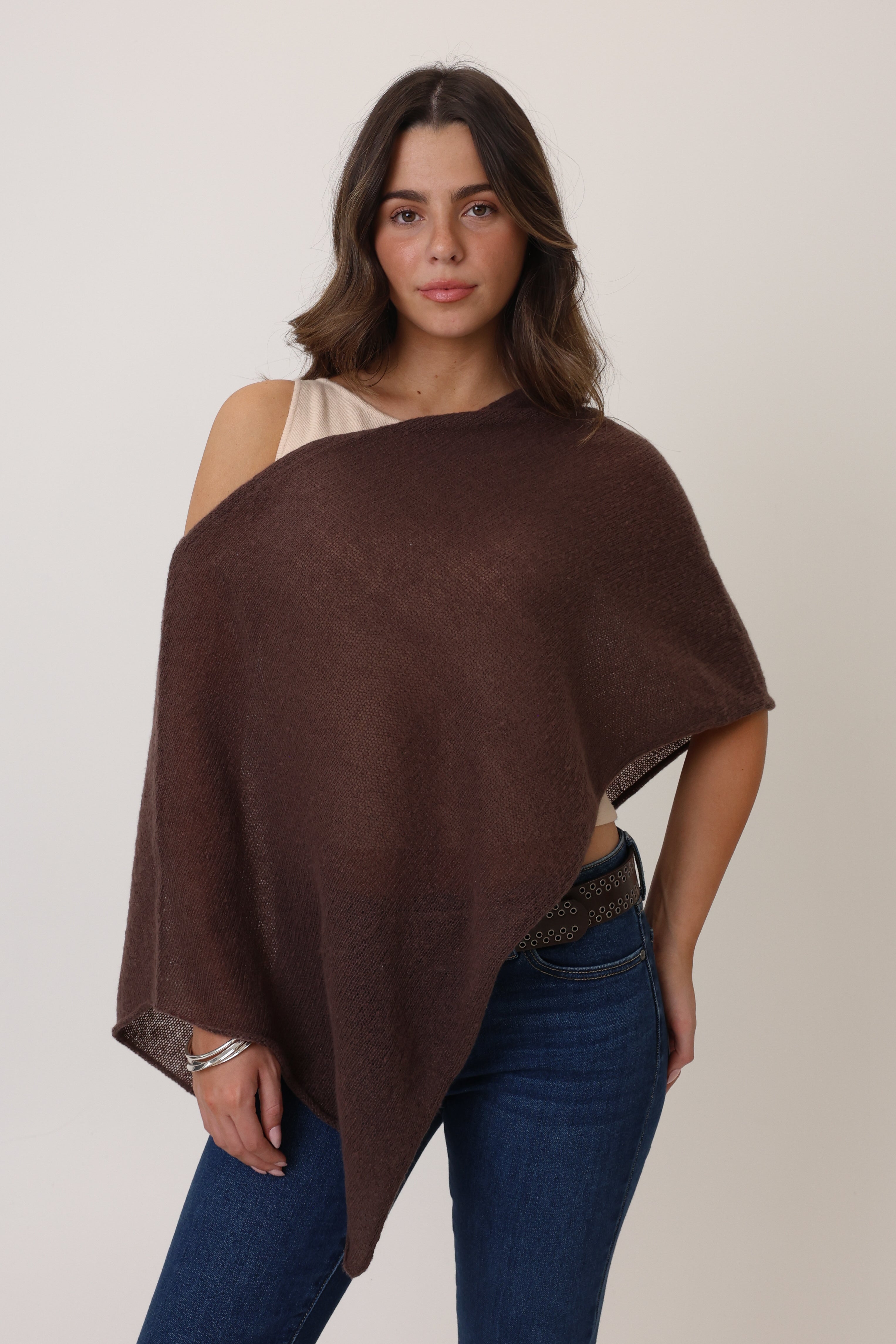 Woman wearing a brown poncho over a beige top and blue jeans on a plain background