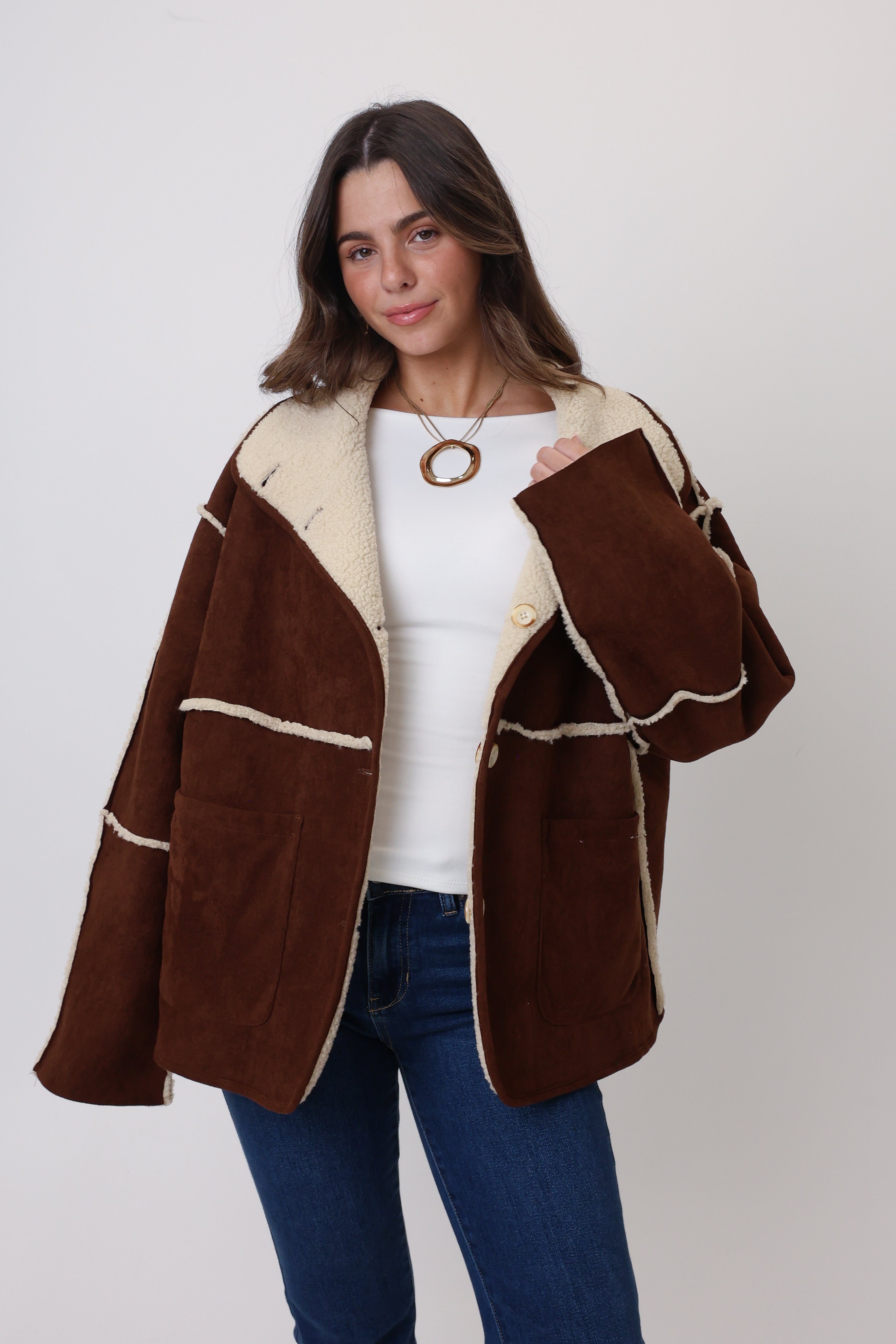 Woman wearing a brown jacket with white trim on a plain background