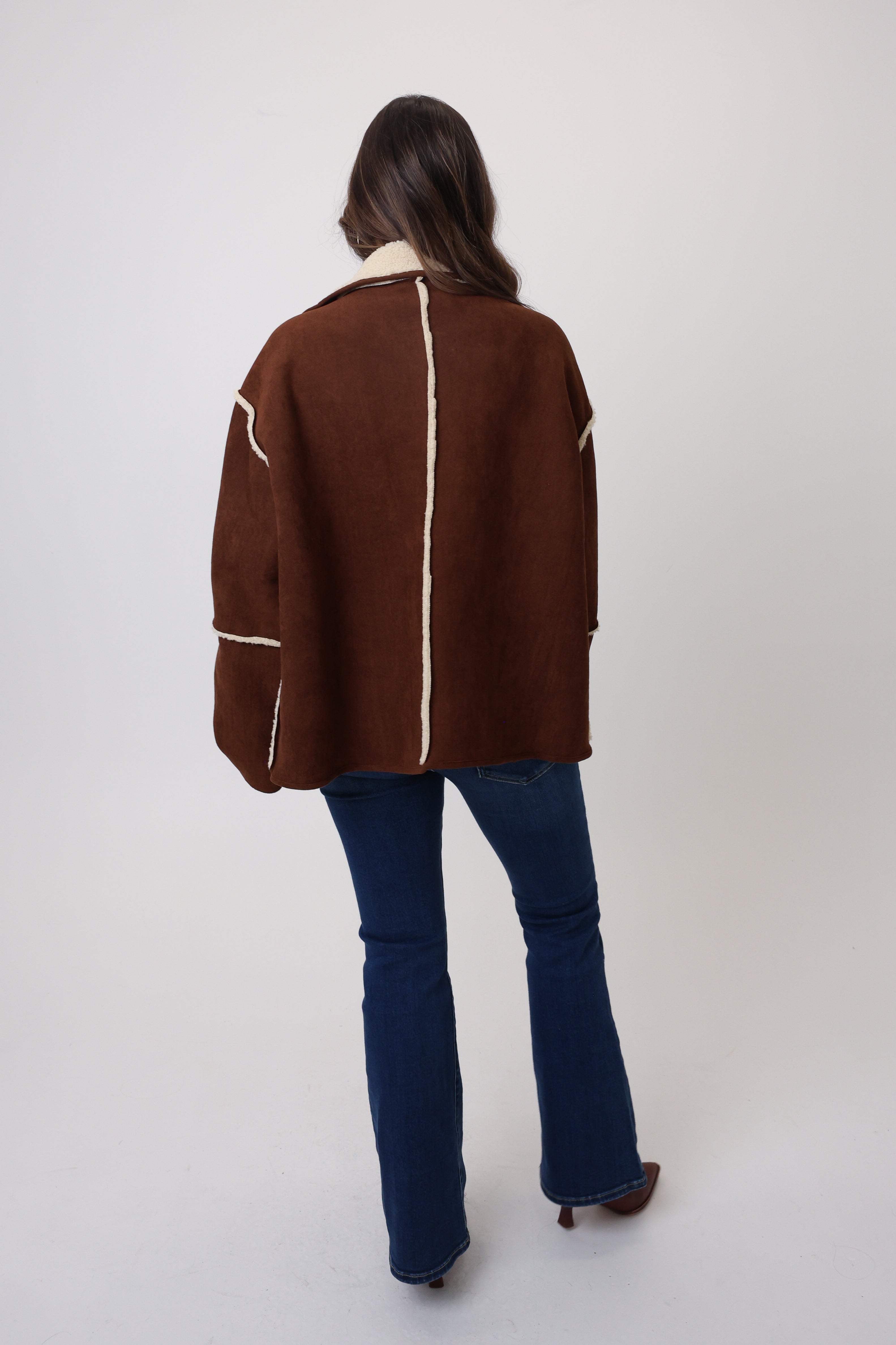 Person wearing a brown jacket with white accents on a plain background