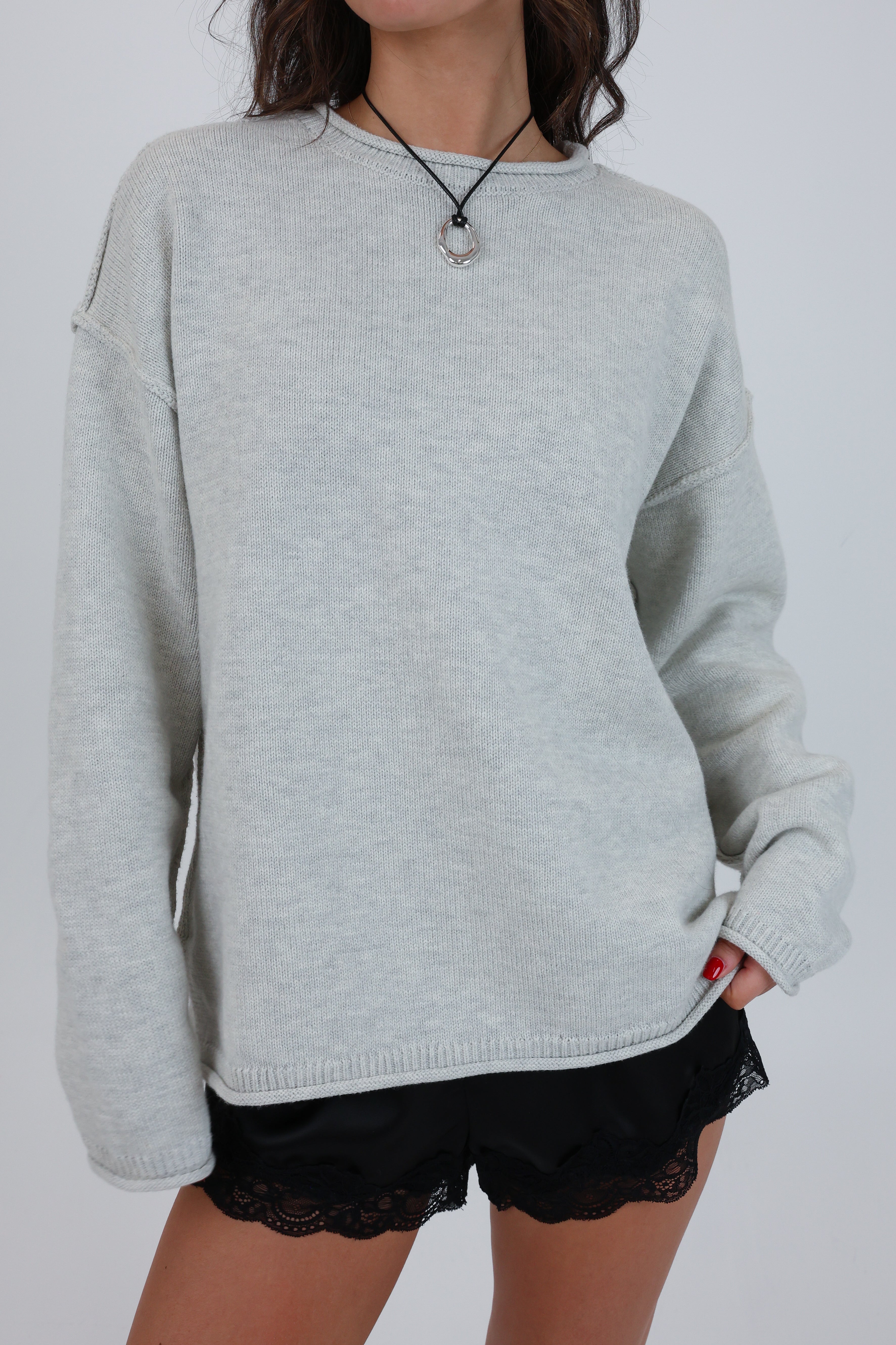 Person wearing a light gray sweater and black shorts on a white background