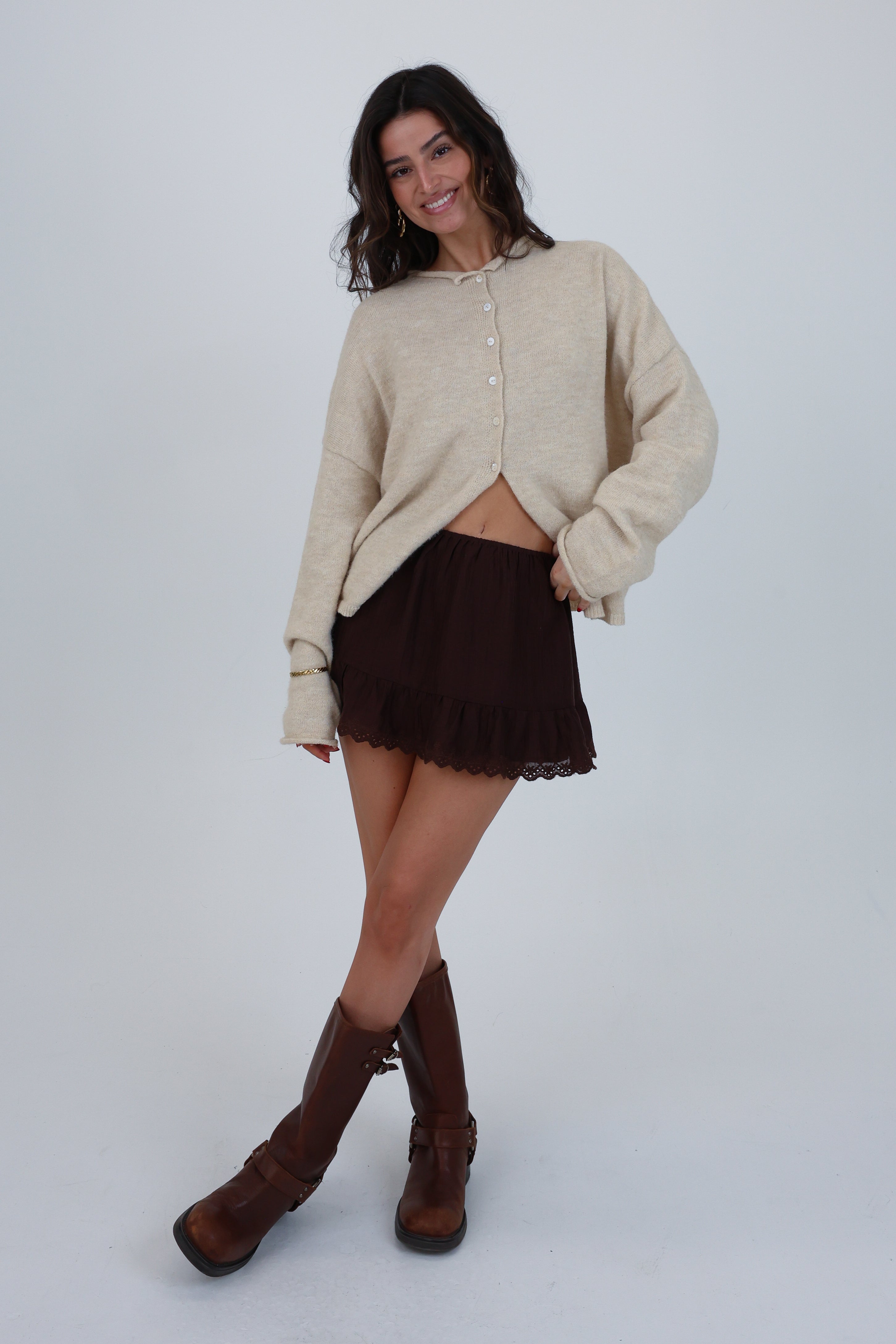 Woman wearing a beige cardigan, brown skirt, and brown boots on a white background