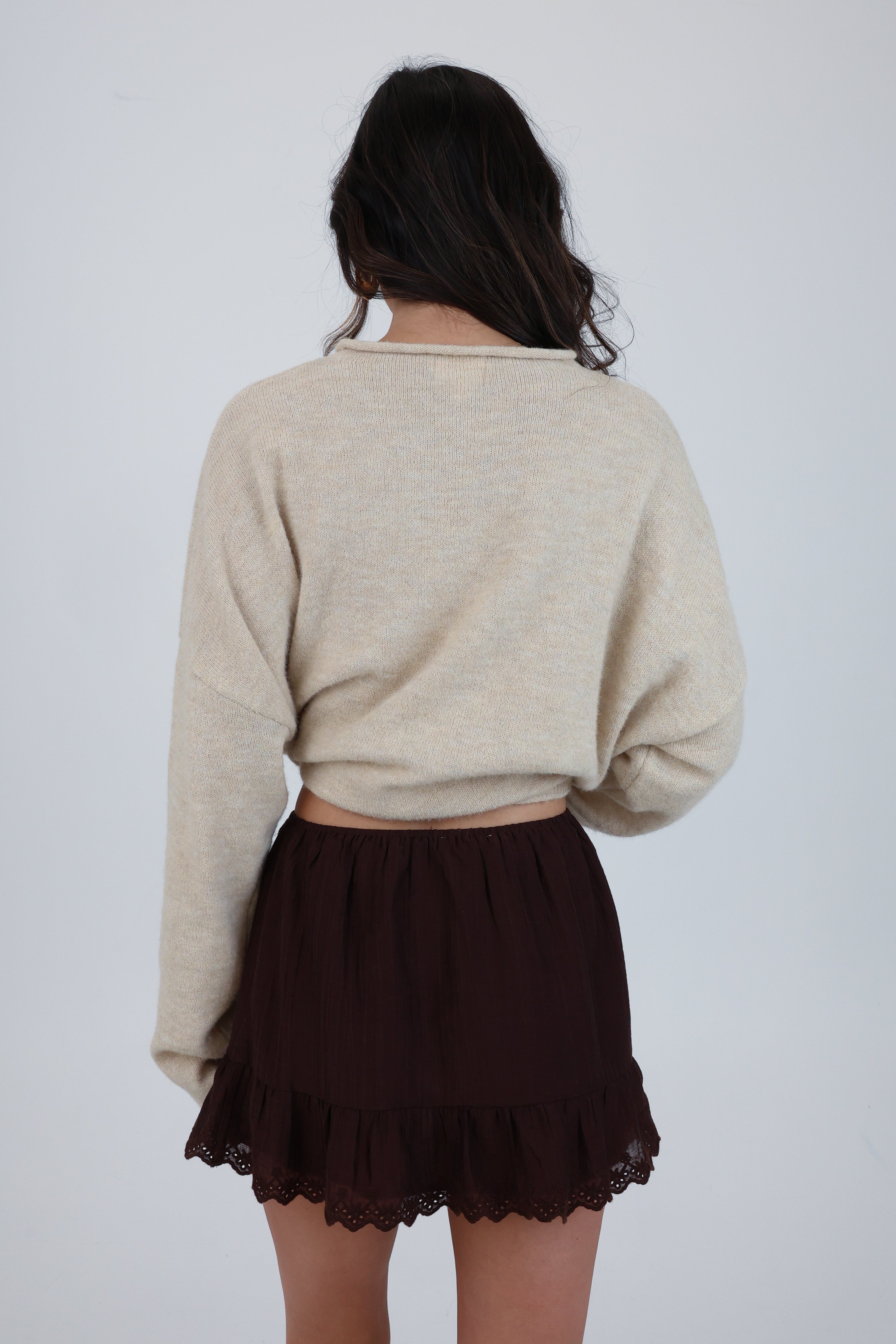 Person wearing a beige sweater and brown skirt on a plain background