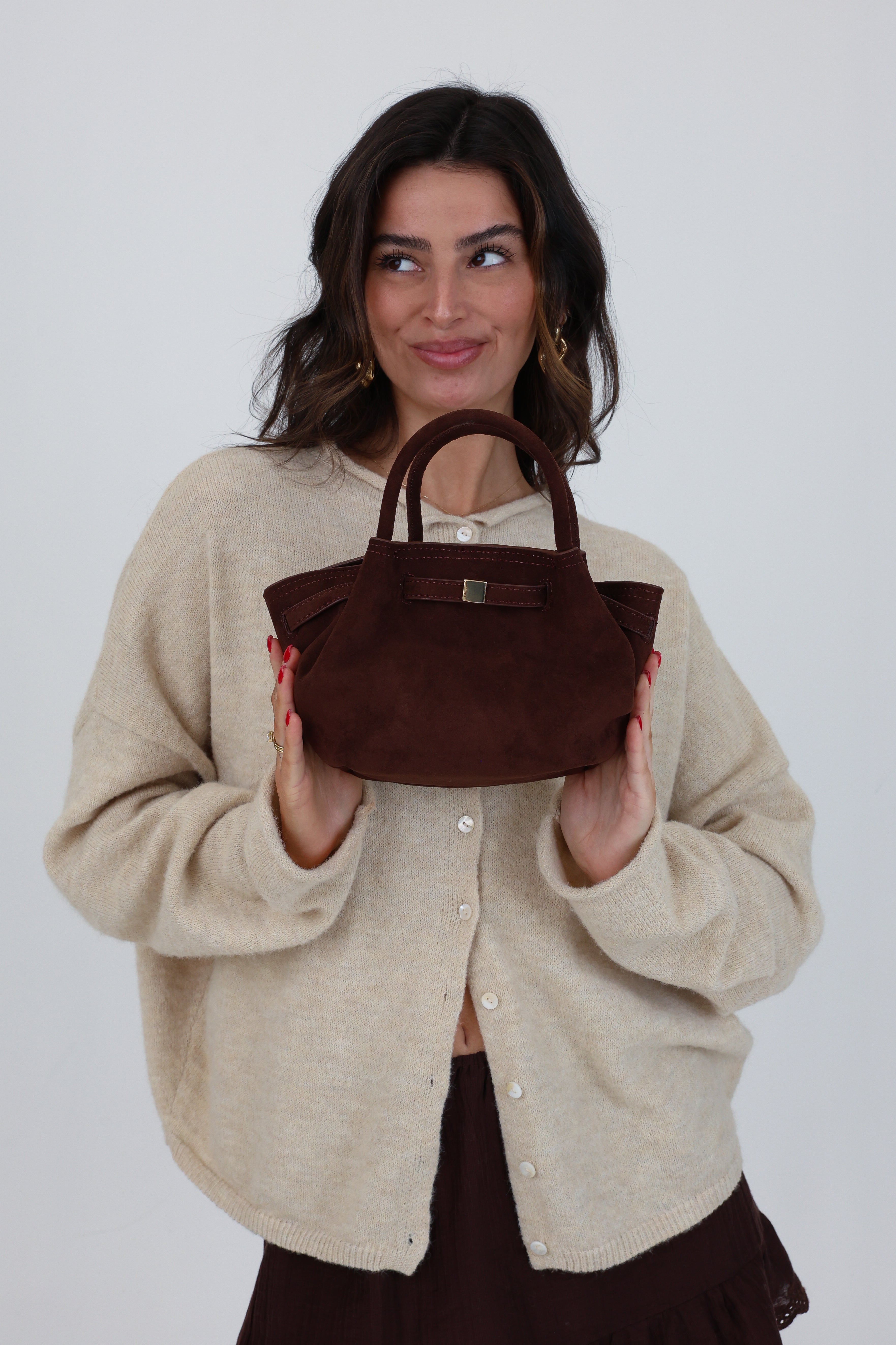 Woman holding a brown handbag against a plain background