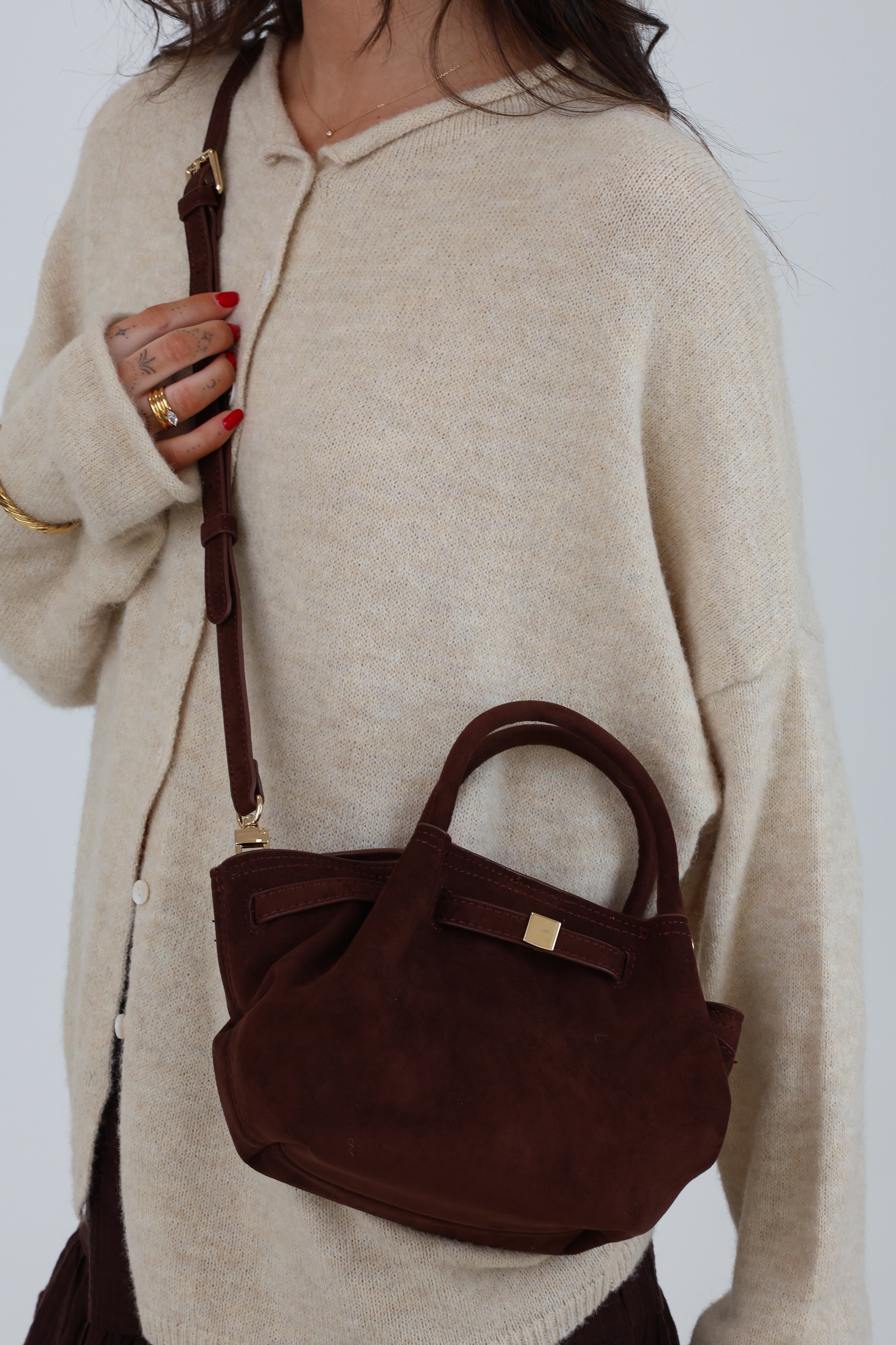 Person wearing a beige sweater holding a brown handbag against a white background