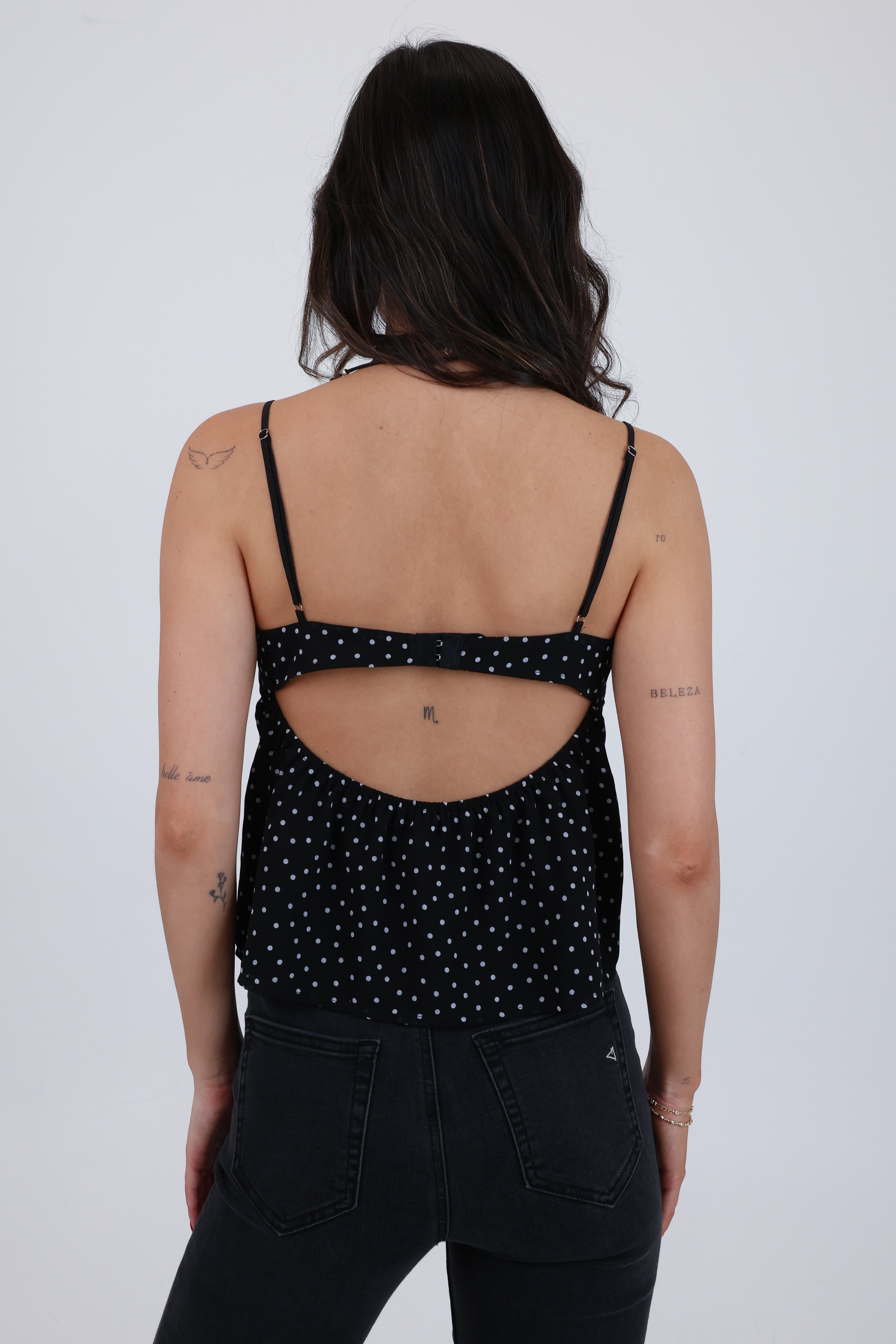 Person wearing a black polka dot tank top with open back on a white background