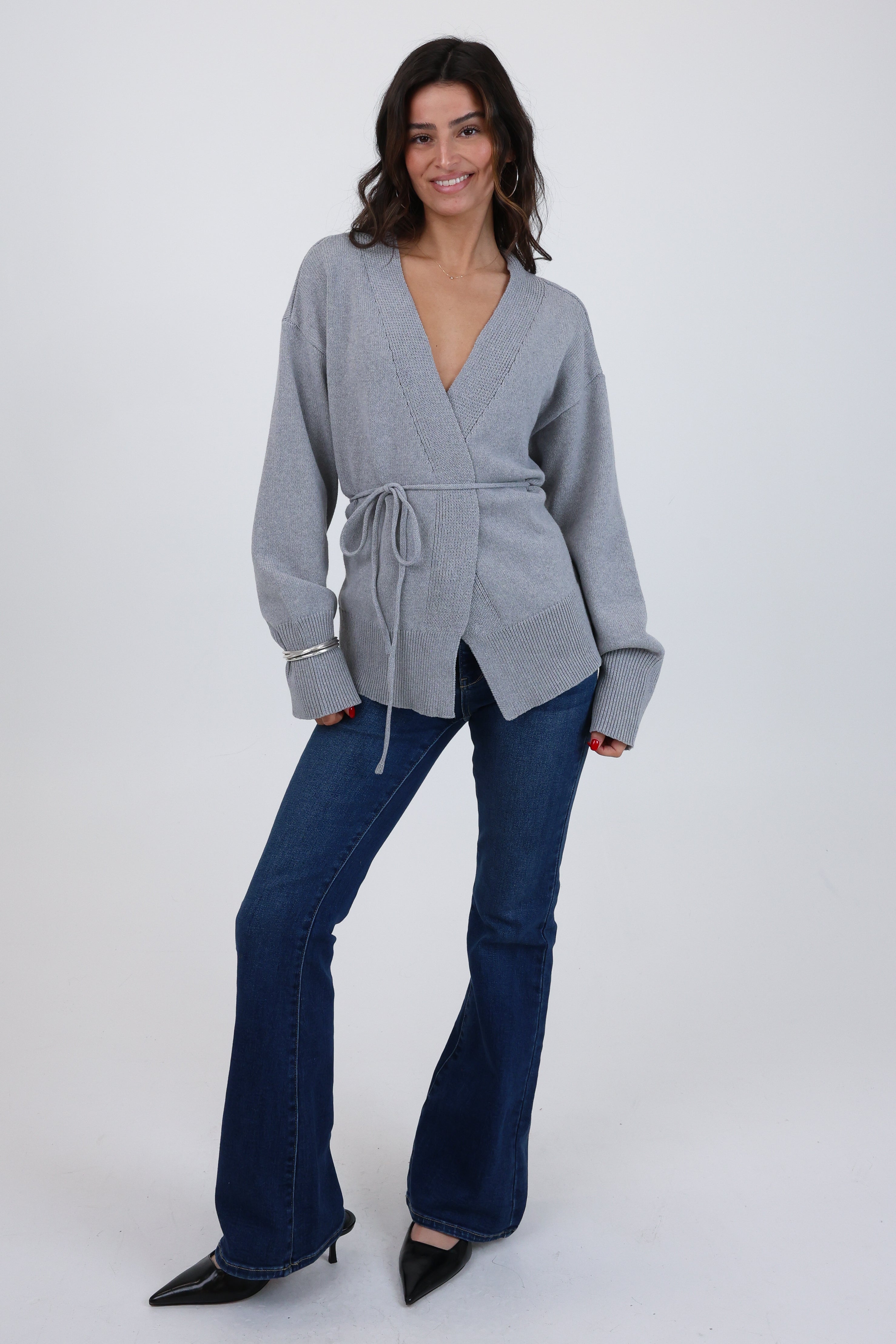 Woman wearing a gray wrap top and blue jeans on a white background