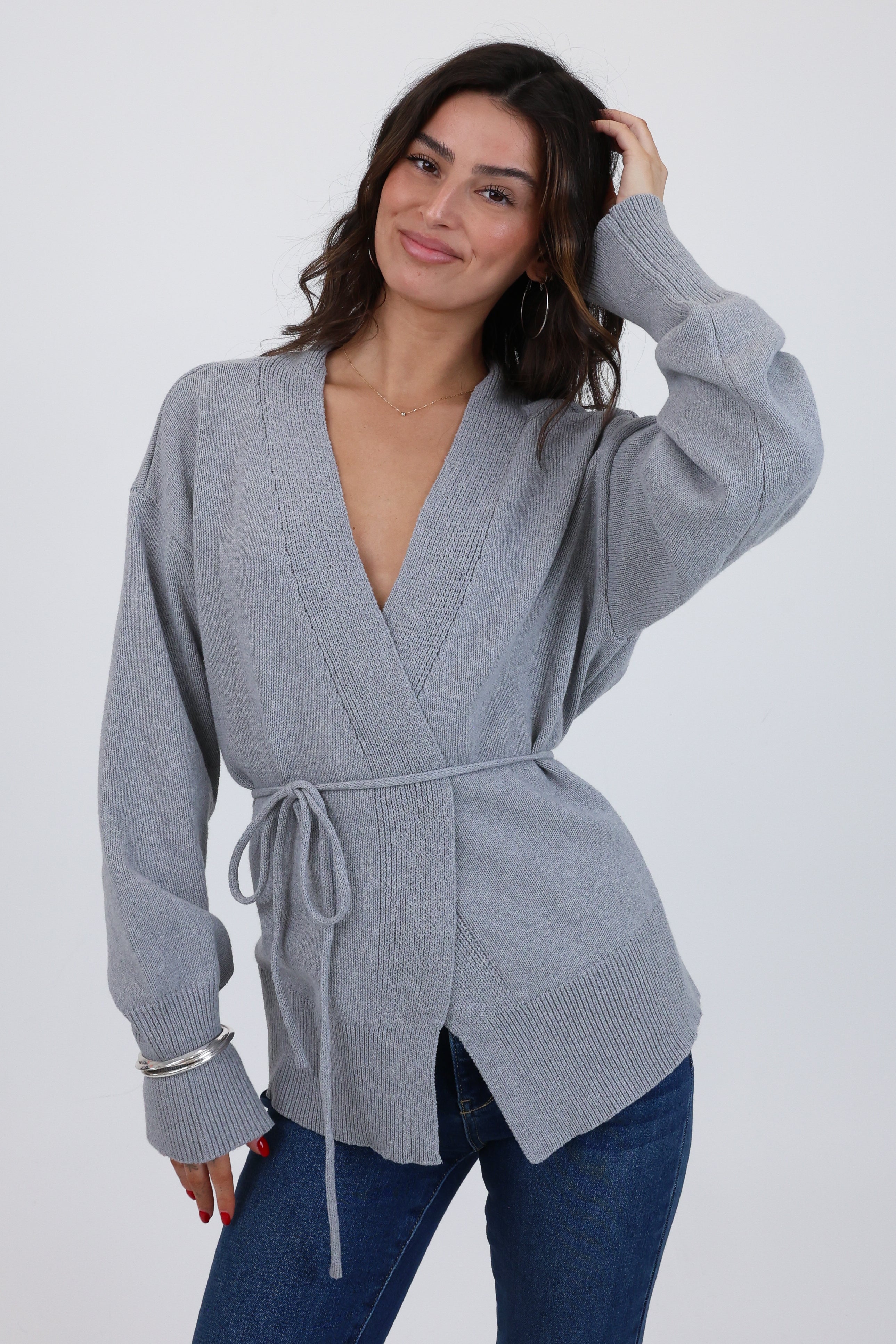 Woman wearing a gray wrap sweater with a plain background