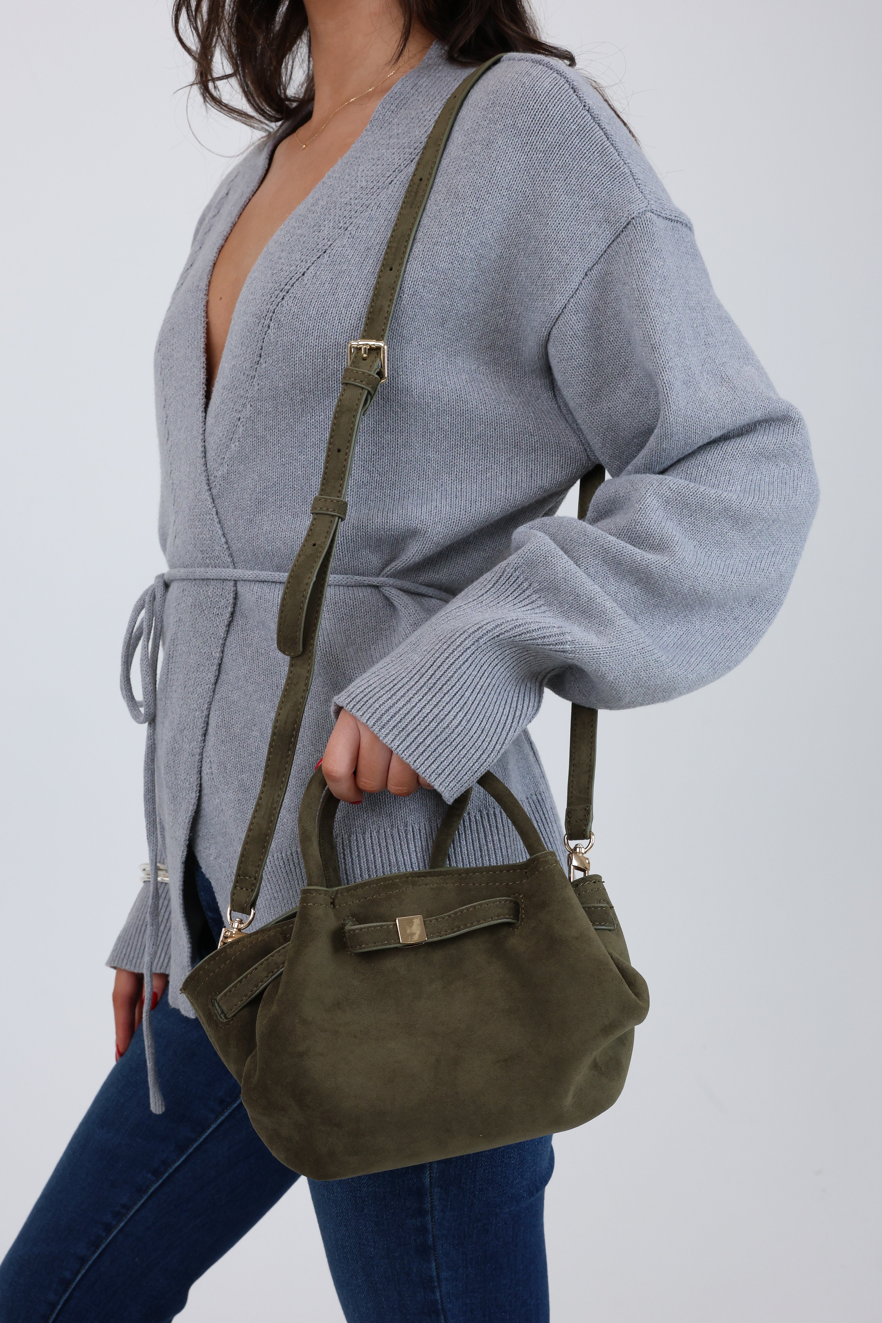 Person wearing a gray cardigan and holding an olive green handbag against a white background