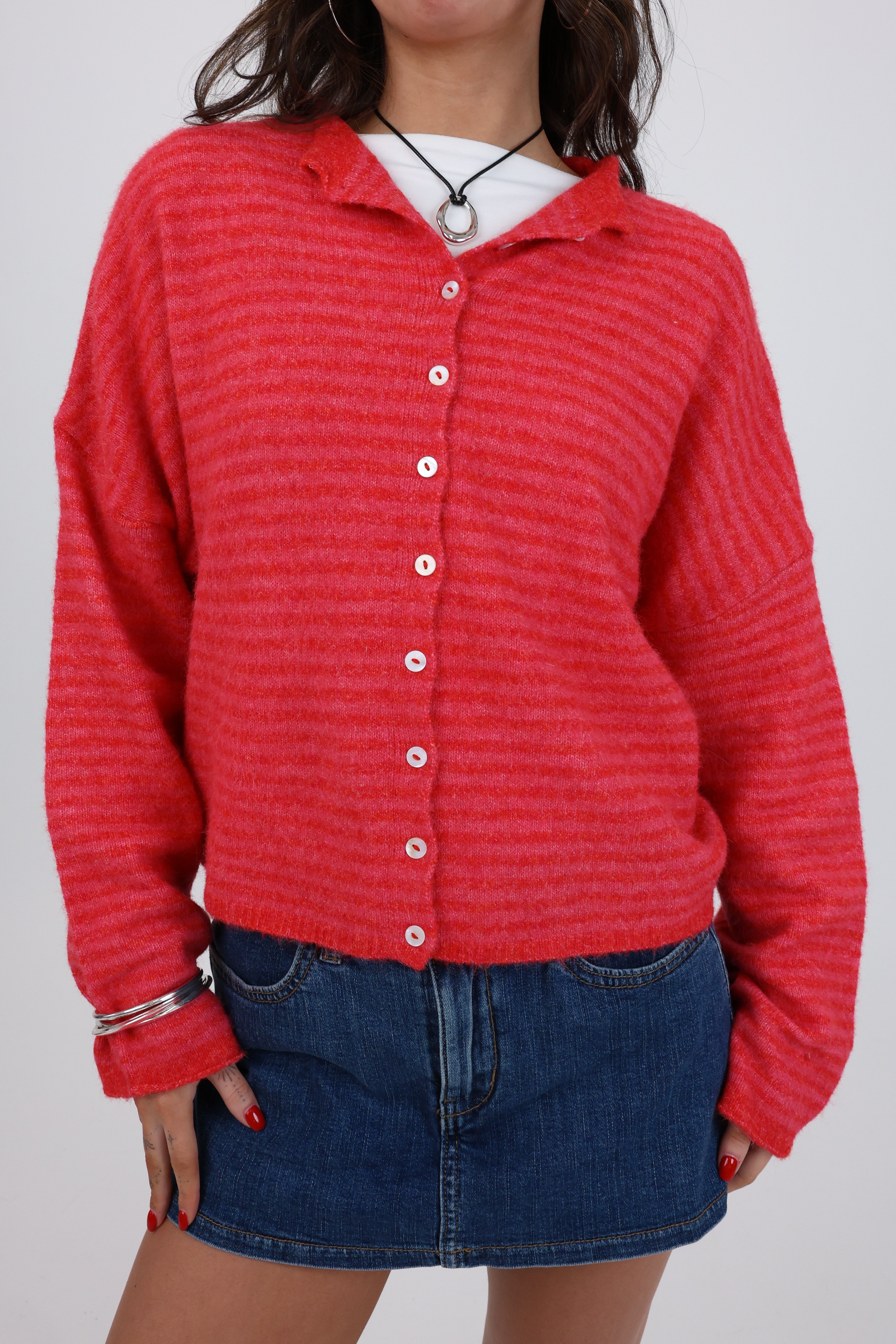 Person wearing a red textured sweater over a white shirt with a blue denim skirt on a plain background