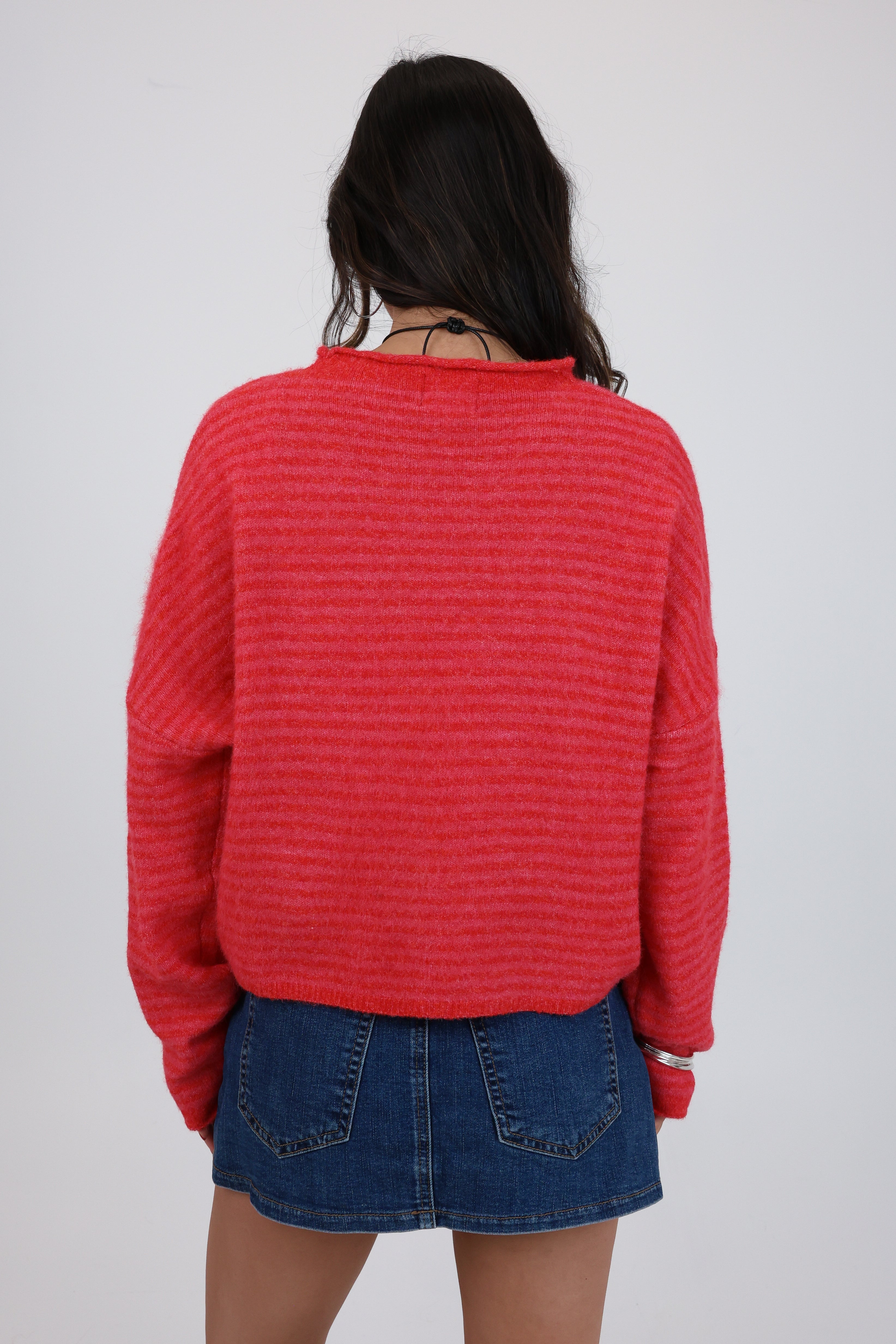 Person wearing a red textured sweater and blue denim skirt on a white background