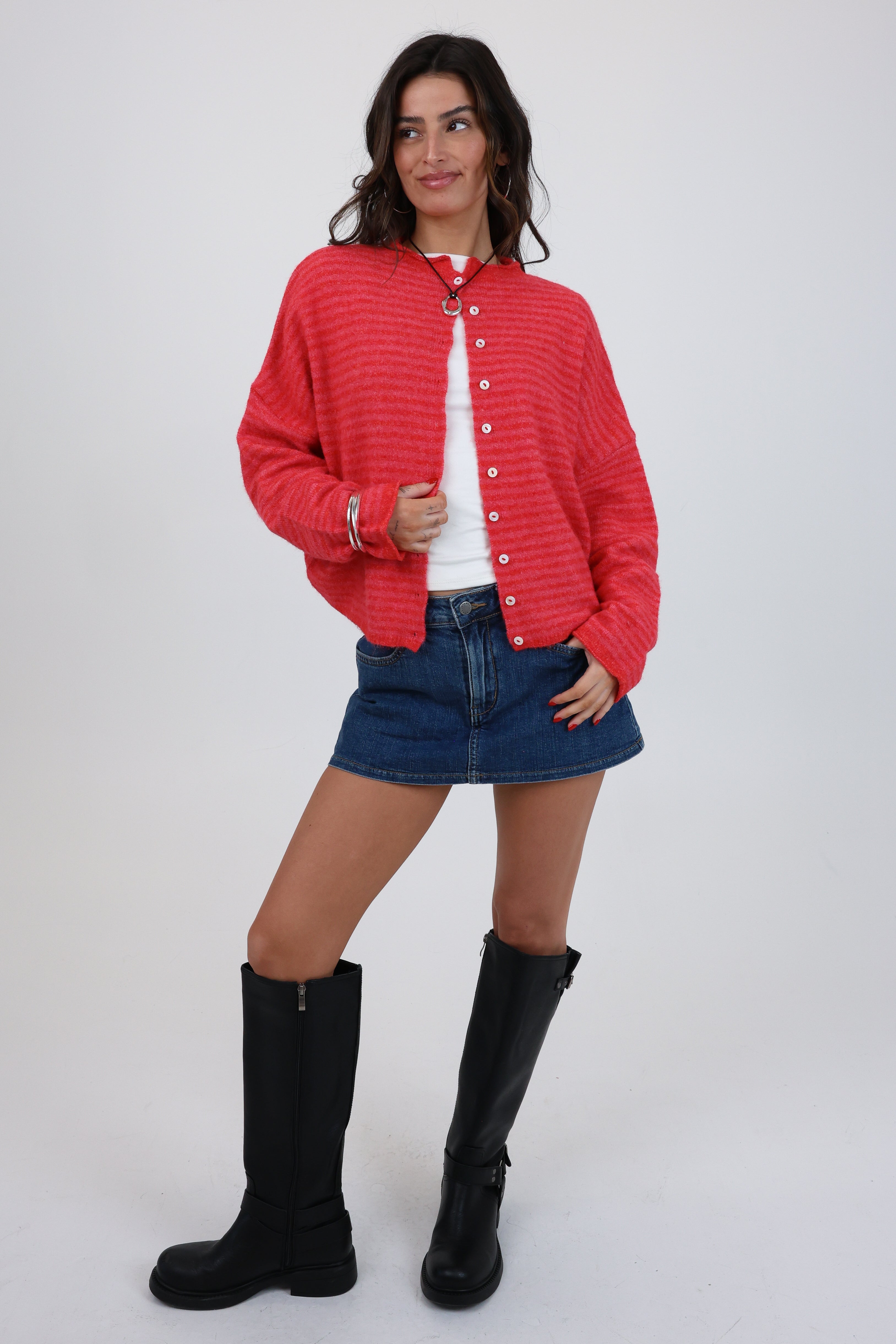 Woman wearing a red cardigan, white shirt, denim skirt, and black boots on a white background