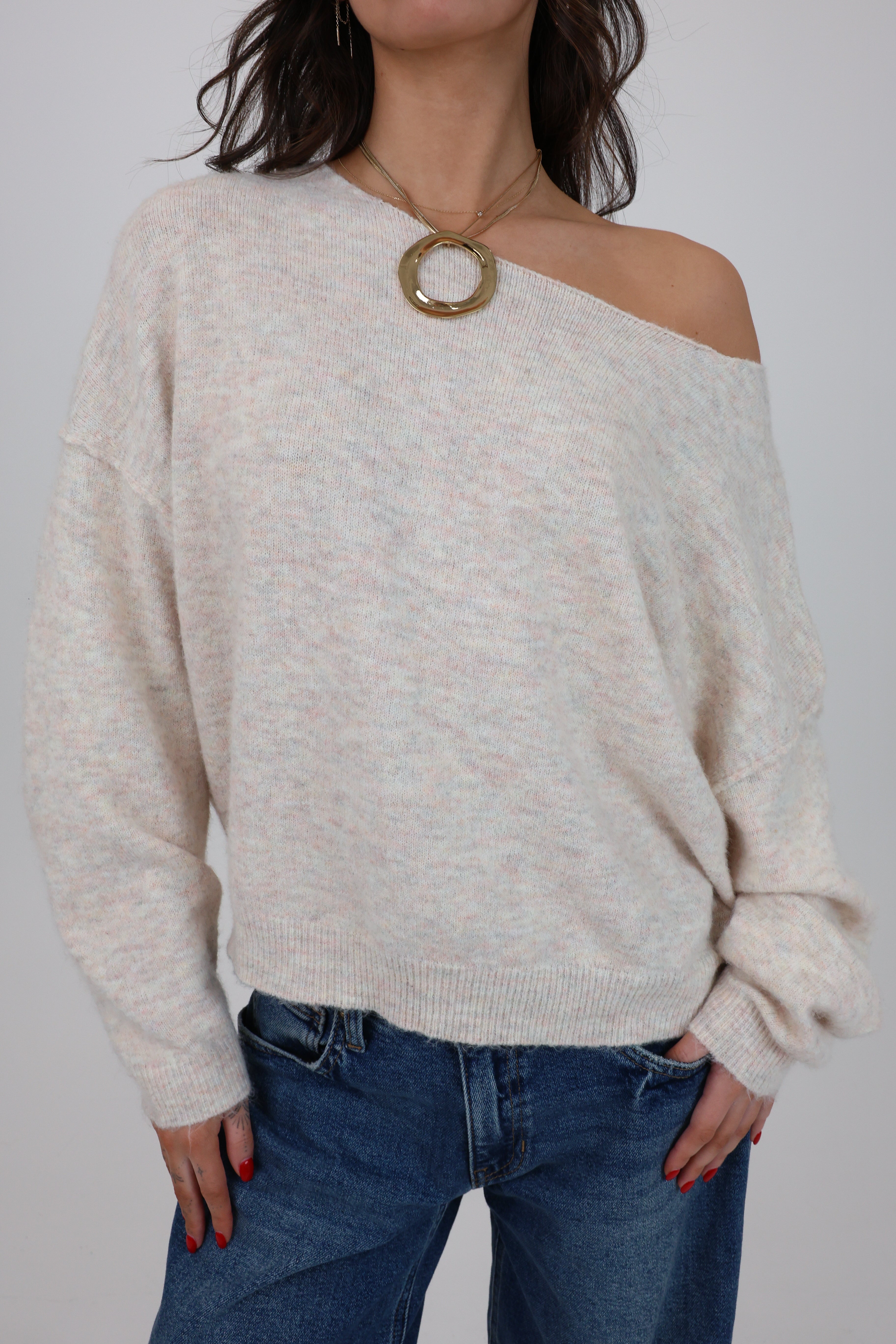Person wearing a beige off-shoulder sweater and blue jeans against a plain background