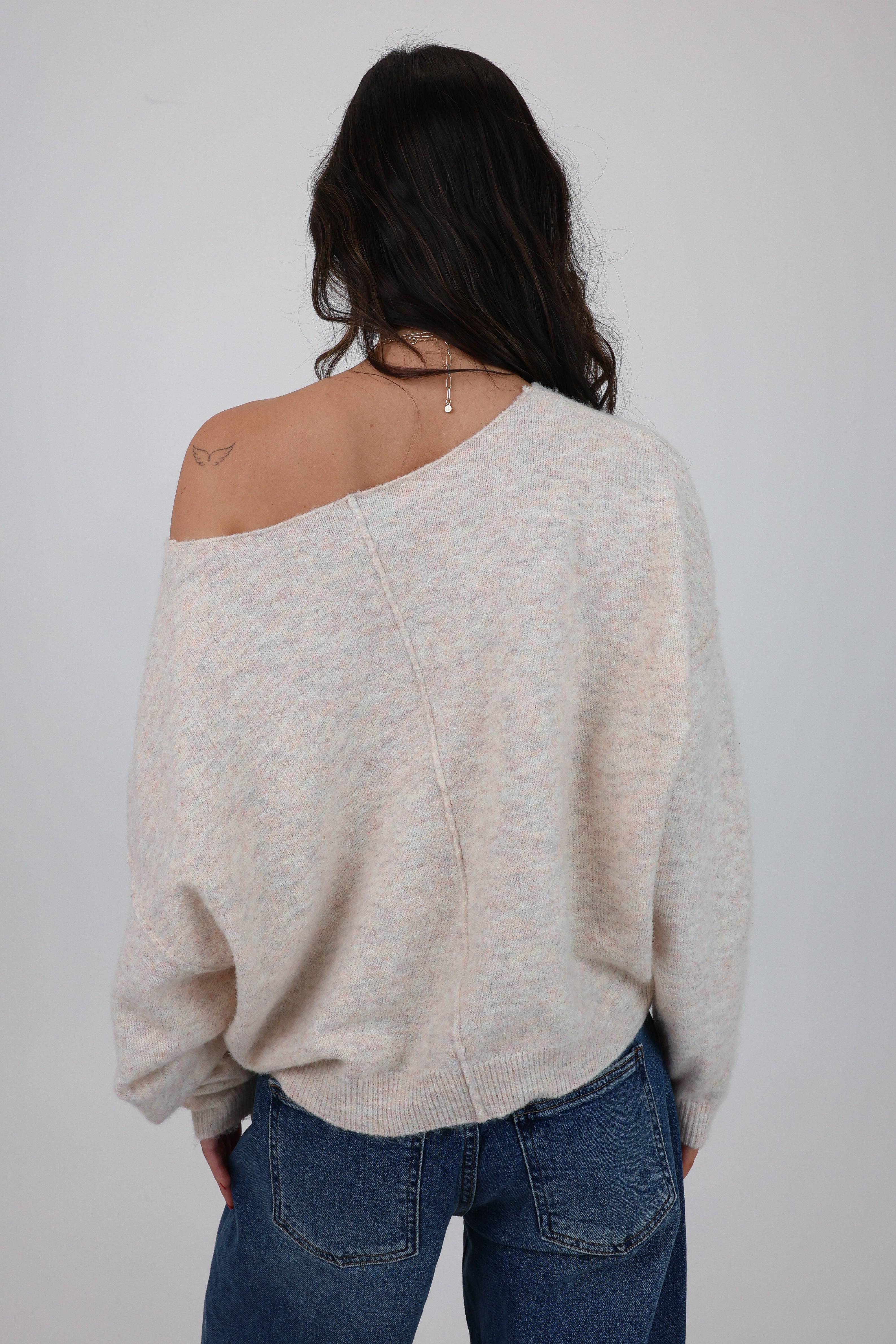 Person wearing a beige sweater and blue jeans against a plain background